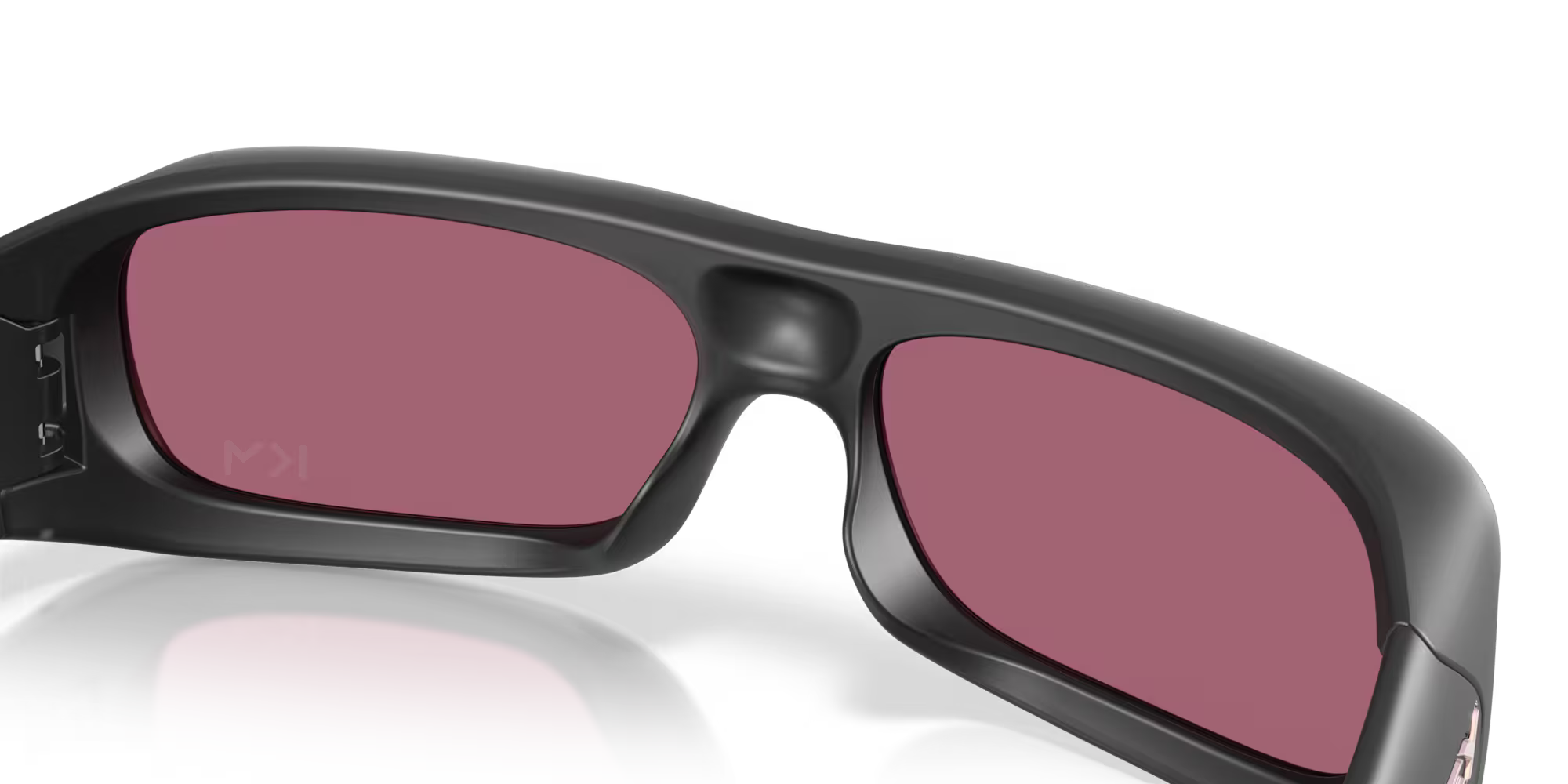 A close-up of the Machina Kylian Mbappé Signature Series Permian sunglasses, featuring black frames and red-tinted lenses with a subtle KM mark on the left lens, shown from behind against a white background.