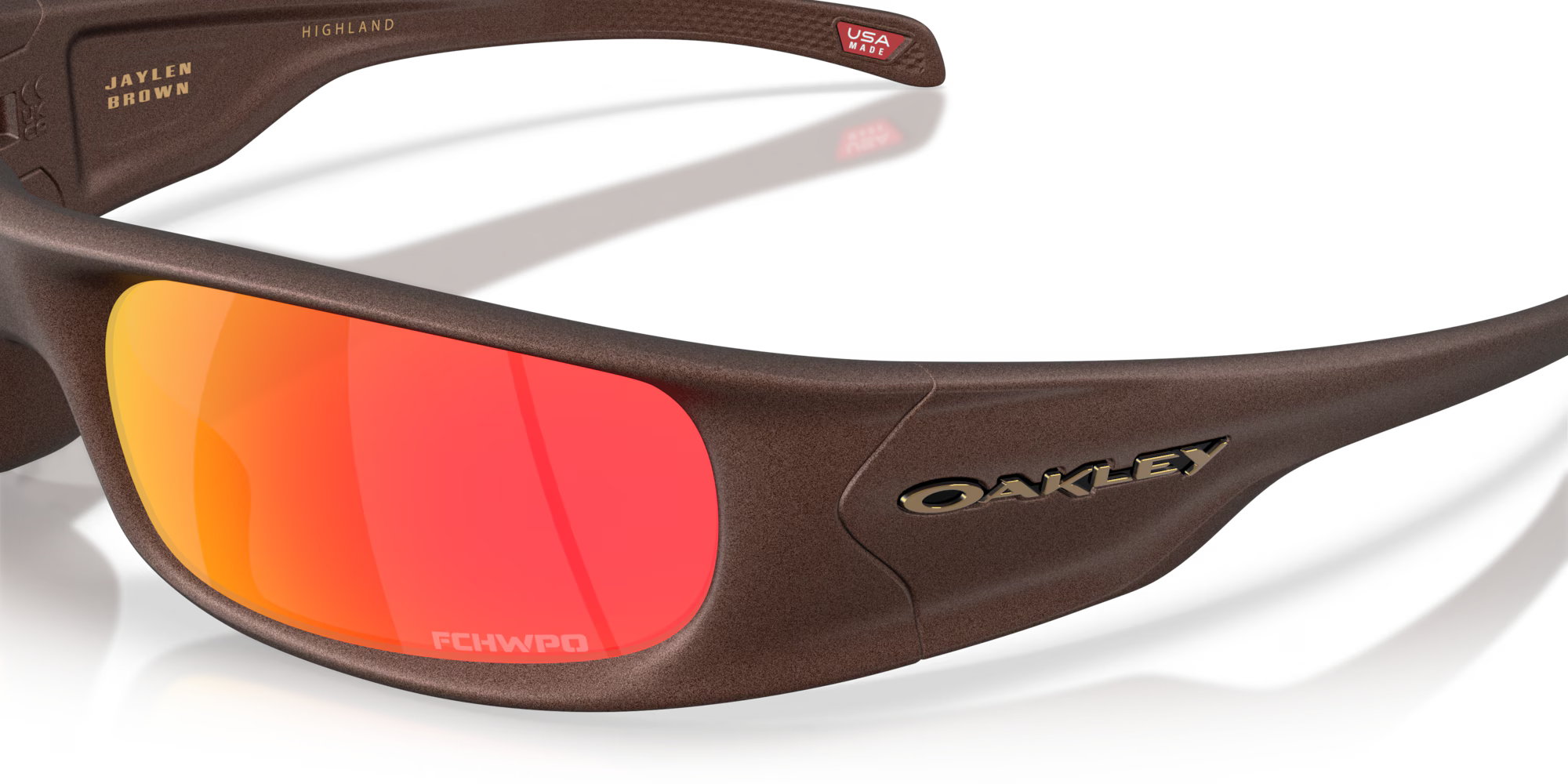 Close-up of brown Machina Highland Jaylen Brown Signature Series eyewear featuring orange-red reflective lenses, engraved JAYLEN BROWN and FCHWPO on the frame, and a small USA sticker—part of the Jaylen Brown collection.