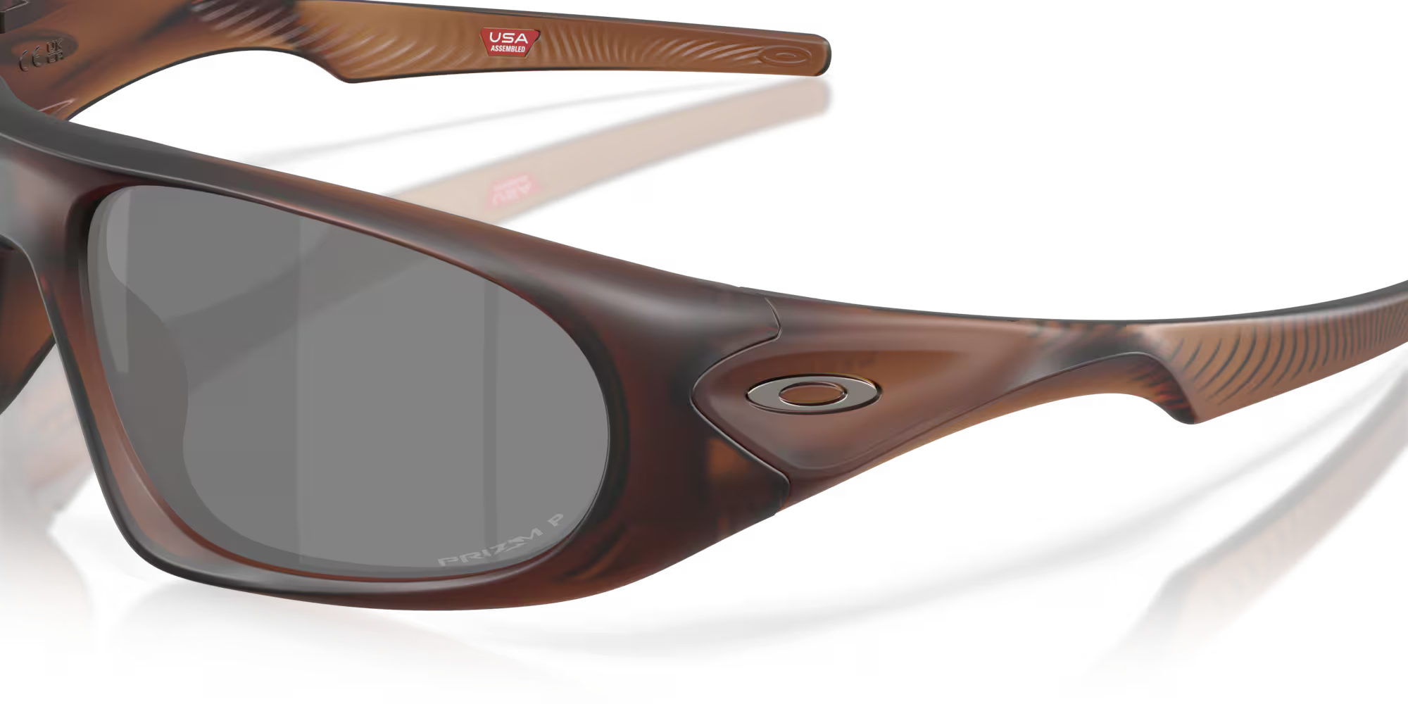 Close-up of Machina - Wearable Technology Neoforma Matte Rootbeer sunglasses with dark lenses, textured frame, brand logo on the side, high-wrap curves, and a small red USA sticker on the inside temple.