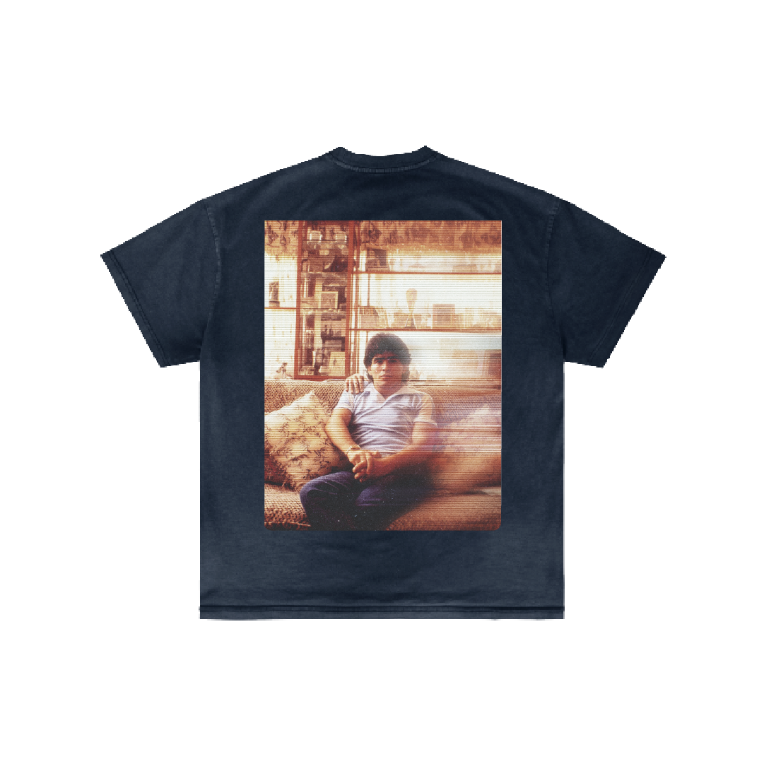 The Diestra y Siniestra T-shirt by Machina - Wearable Technology features a large photo on the back of a person on a couch in a vintage, warmly lit room with subtle religious iconography woven into the scene.