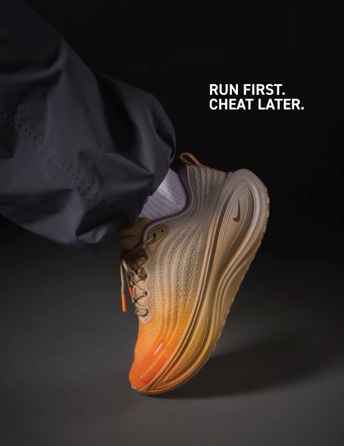 A close-up of a foot wearing an orange and beige PAINANIS DEL ASFALTO sneaker by Machina Wearable Technology, emblazoned with the text RUN FIRST. CHEAT LATER. on a dark background.