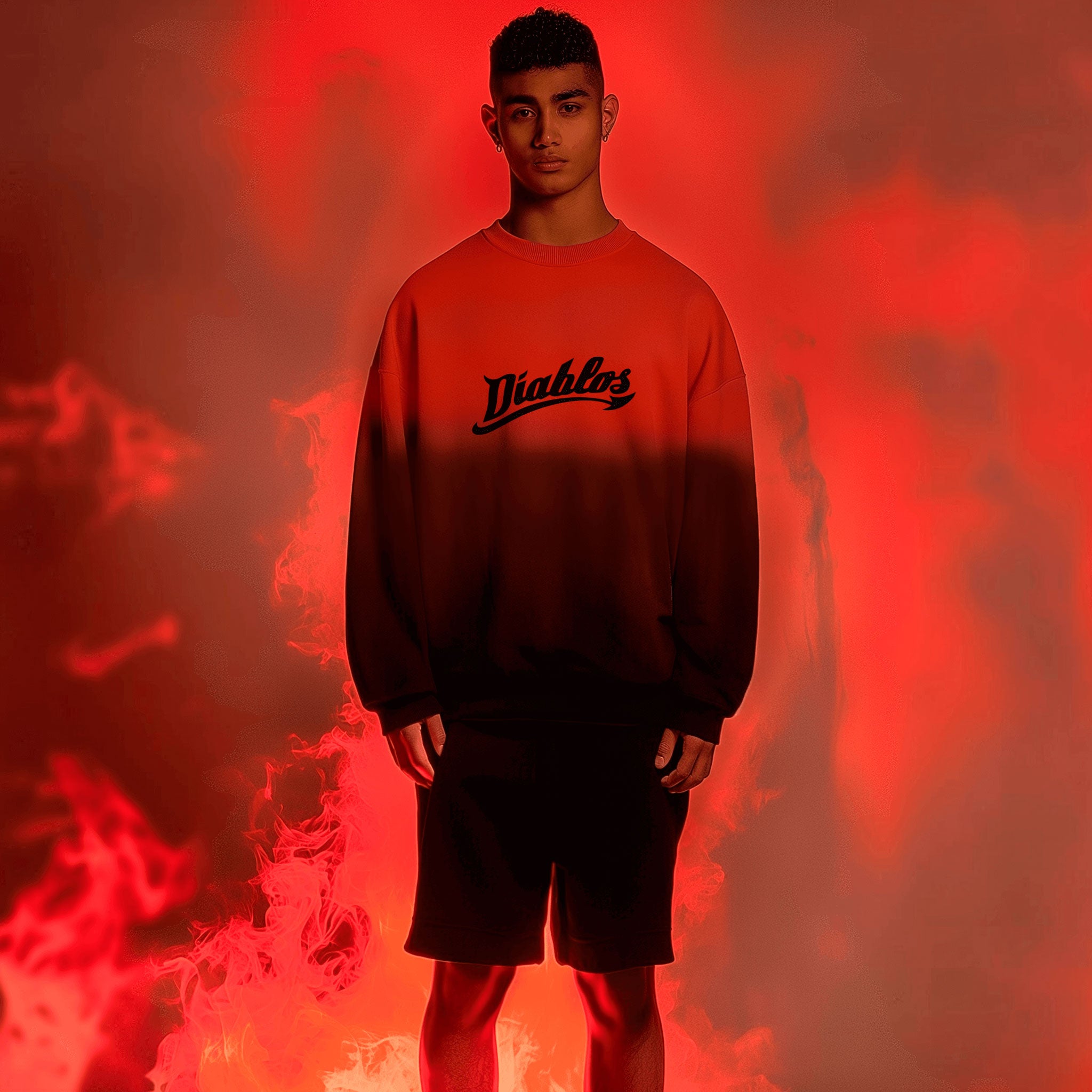 A young man stands engulfed by red and orange flames, wearing the limited edition Crimson Crewneck from Machina - Wearable Technology, featuring Diablos on the front, paired with black shorts. The fiery backdrop heightens the drama of the scene.