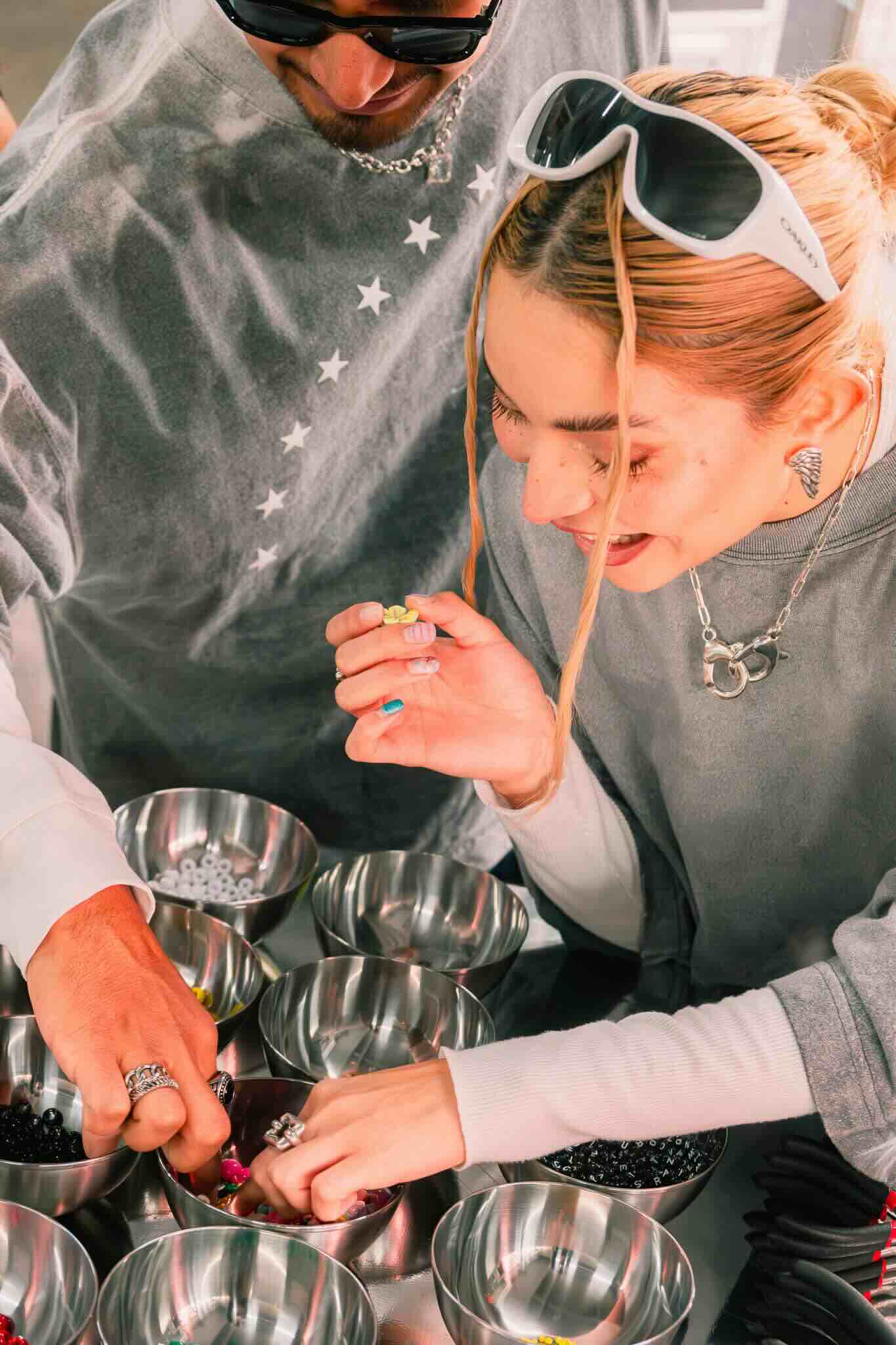 At the OUROBOROS DIY CHARM WORKSHOP by Machina Wearable Technology, two people in gray shirts smile as they select vibrant beads, creating unique custom jewelry during an interactive session.