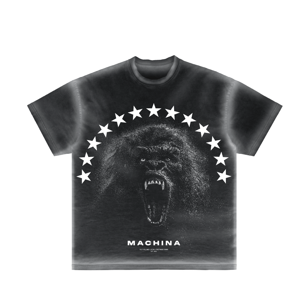 A predominantly black T-shirt with a faded effect, named "El Protector," showcases a graphic of a roaring gorilla enveloped in the enigmatic shadows of the forest, encircled by a semi-circle of stars. The shirt features the brand name "Machina - Wearable Technology" printed beneath the image.