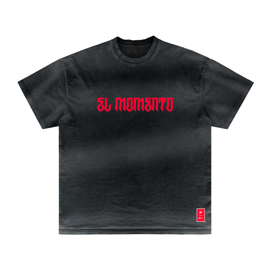 The "El Momento" t-shirt from Machina - Wearable Technology showcases a black design adorned with striking red Gothic-style text on the front, capturing an essence reminiscent of Japanese culture. At the bottom hem, a small red tag featuring additional text adds an enigmatic touch of yokai mystique.