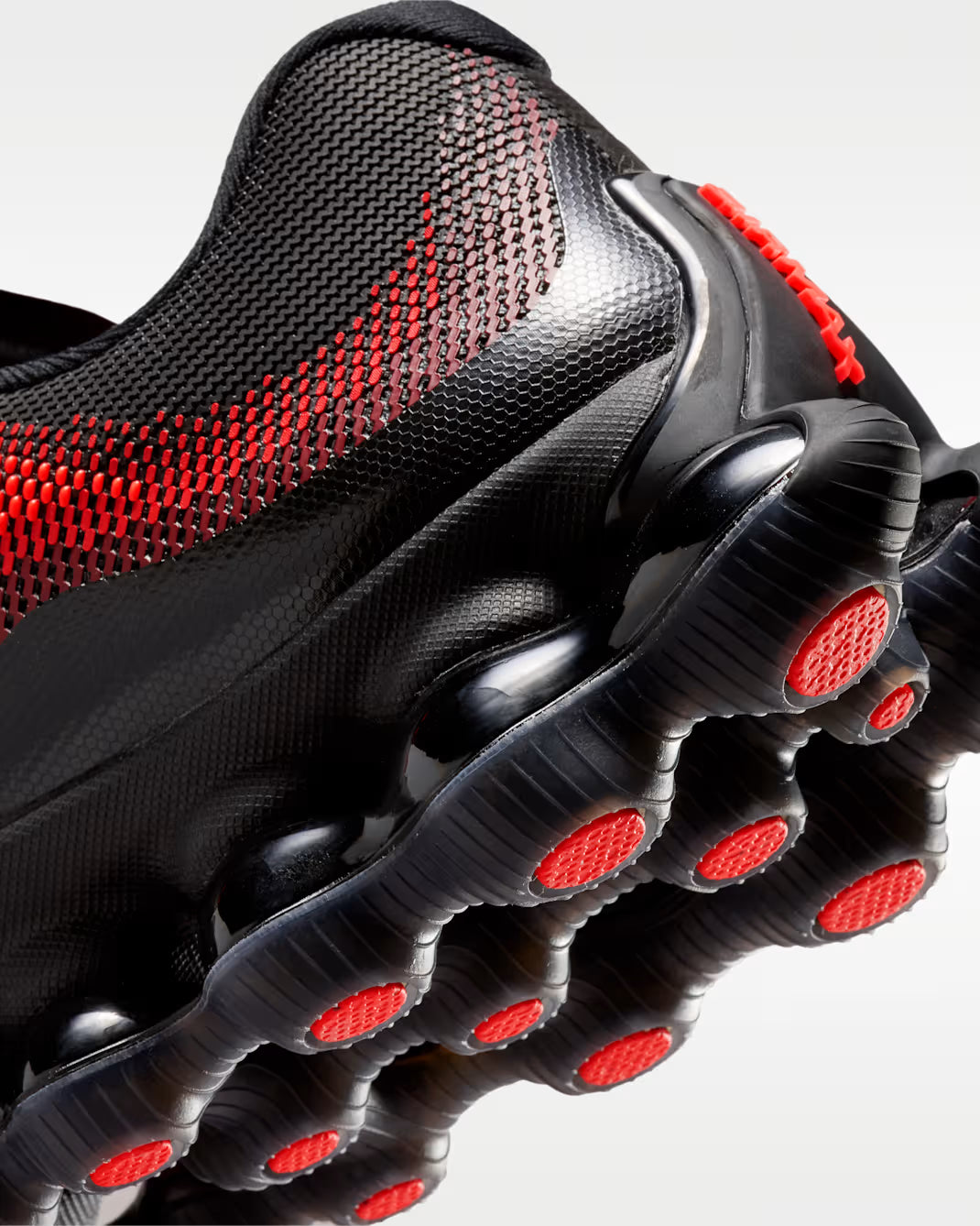 Close-up of the Machina Wearable Technology Air Liquid Max 'Bright Crimson Fire Red,' a black athletic shoe with a textured mesh upper, bold red accents, and the signature sole featuring raised circular pods, some highlighted in red.