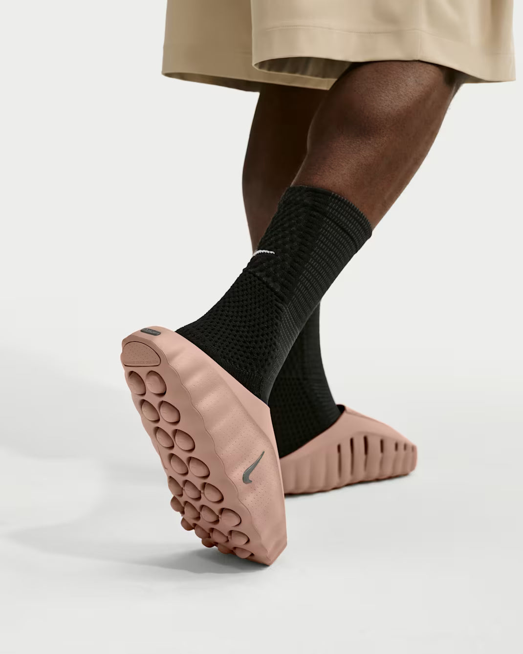 Person wearing black crew socks and blush pink Mind 001 sensory sneakers with a molded, pill-shaped tread pattern on the soles.