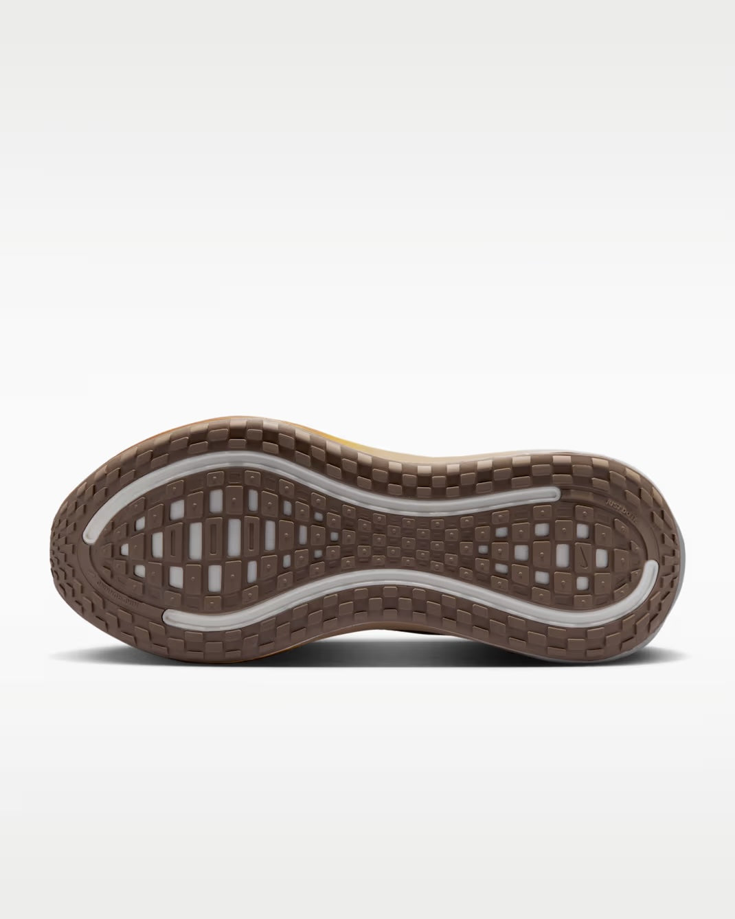 The image shows the brown rubber outsole of a Nike Vomero Plus “Cheat Day” running shoe by Machina Wearable Technology, featuring a textured tread pattern with rectangular and oval shapes and white accents along the sides for enhanced grip and traction.