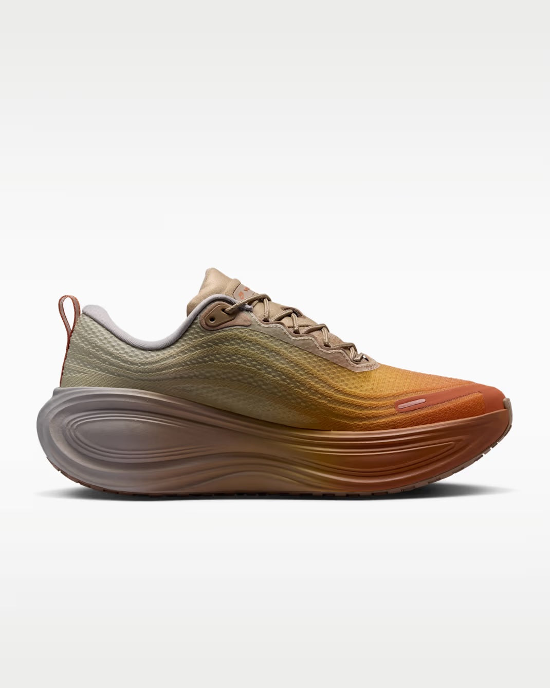 A single Nike Vomero Plus “Cheat Day” running shoe by Machina Wearable Technology, featuring tan, orange, and brown hues with a wavy, thick ZoomX midsole, is displayed in profile against a plain white background.