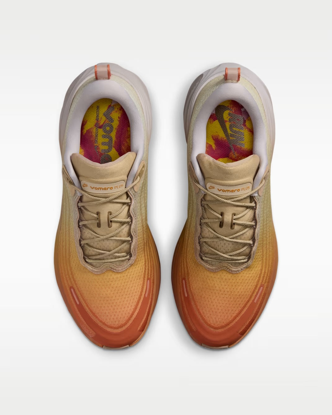 Top view of a pair of Nike Vomero Plus “Cheat Day” sneakers by Machina Wearable Technology in tan and orange gradient with beige laces and yellow-pink insoles, featuring a ZoomX midsole for added comfort, set against a white background.
