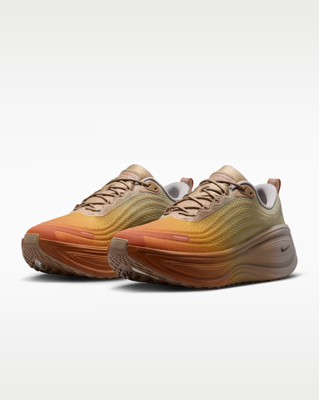 Pair of Nike Vomero Plus “Cheat Day” running shoes by Machina Wearable Technology featuring a gradient design that fades from tan at the toe to gold and light brown towards the heel, set against a plain white background.