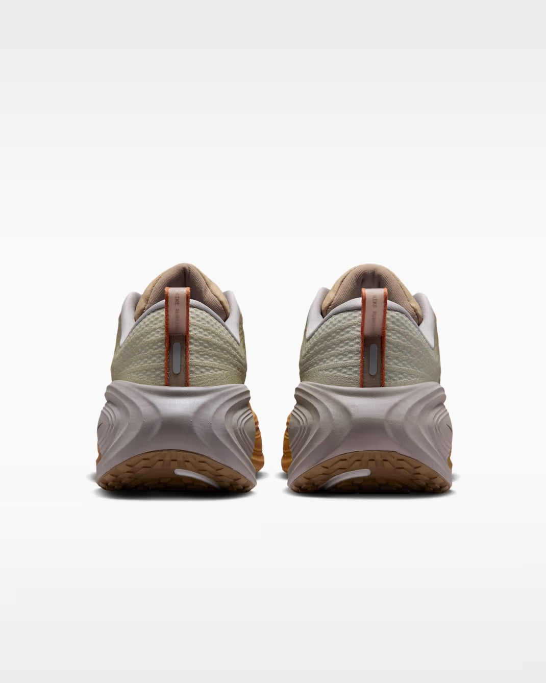 A pair of Nike Vomero Plus “Cheat Day” running shoes by Machina Wearable Technology is shown from the back, featuring textured beige and tan uppers, thick white ZoomX midsoles, brown pull tabs, and gum-colored outsoles on a plain white background.