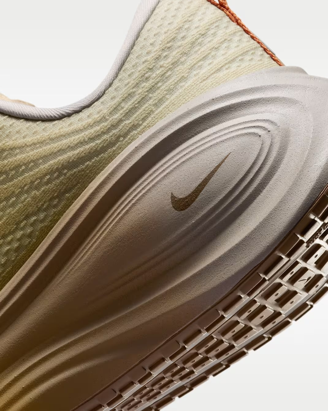 Close-up of the Machina Wearable Technology Nike Vomero Plus “Cheat Day” running shoe, highlighting the textured, light-colored upper, cushioned ZoomX midsole with a small Nike swoosh, and a portion of the outsole tread pattern.