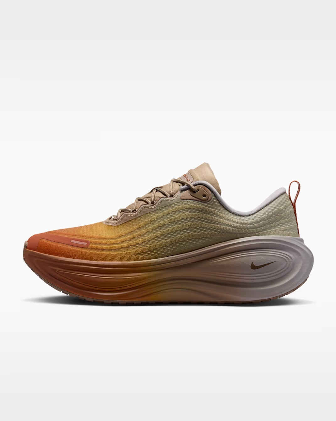 A Machina Wearable Technology Nike Vomero Plus “Cheat Day” running shoe with a gradient design from orange at the toe to beige at the heel, featuring wavy detailing, a thick sculpted ZoomX midsole, and a small Nike logo near the heel.