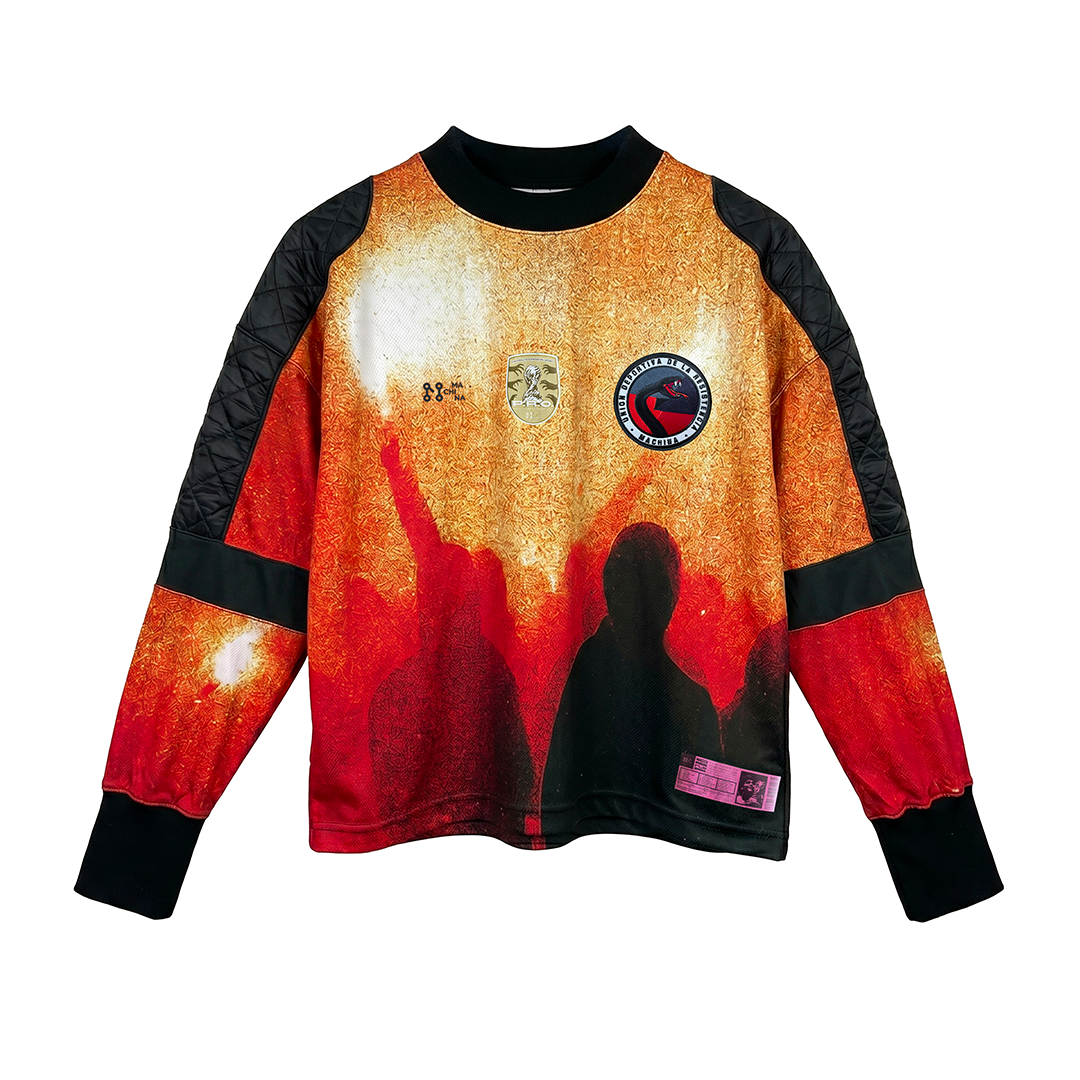 The Vincere o Morire by Machina – Wearable Technology is a long-sleeve shirt with a vivid red-orange crowd scene, black quilted shoulders and cuffs, and two front patches inspired by the 1934 World Cup jersey and anti-fascist resistance.
