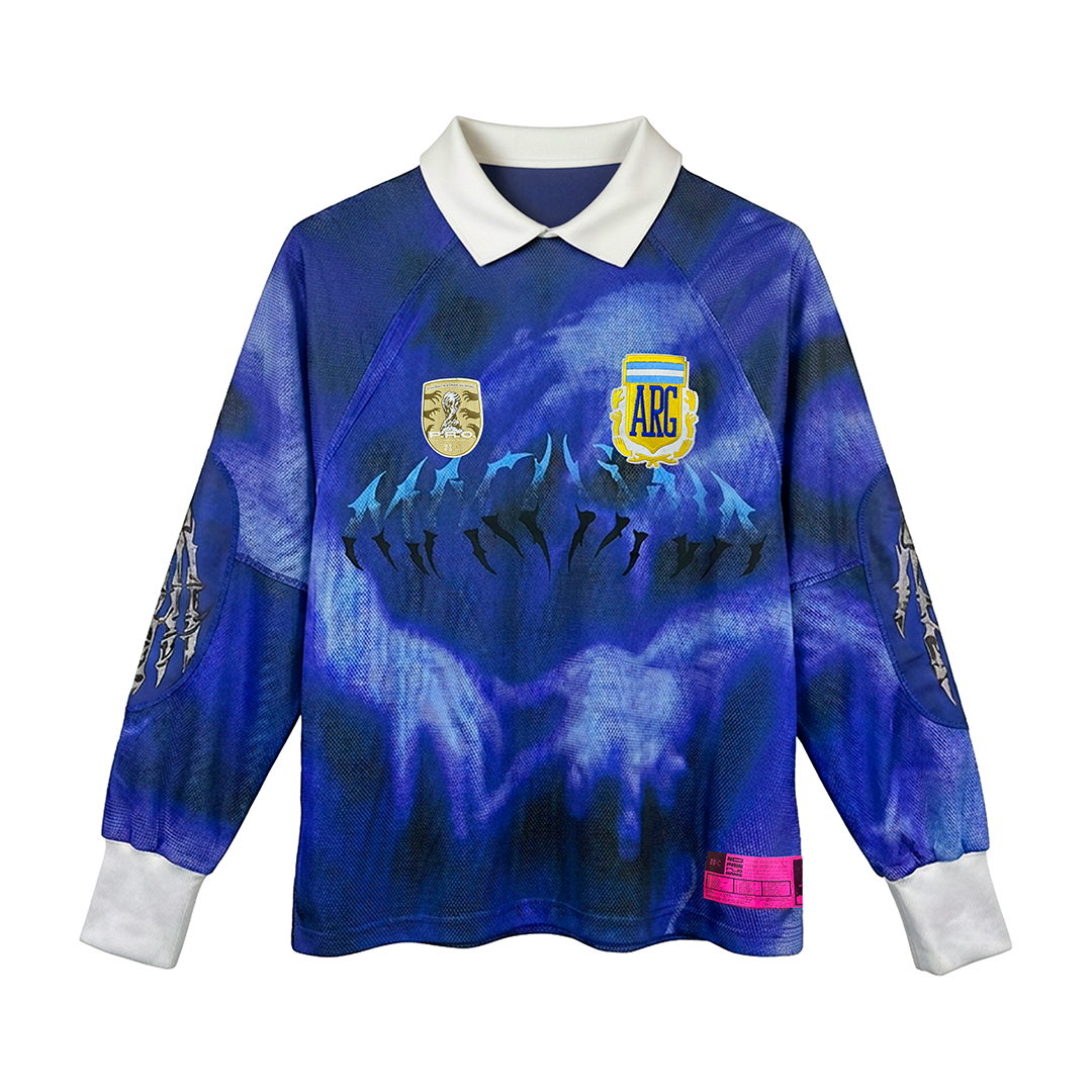 The LA MANO DE DIOS LS by Machina - Wearable Technology is a long-sleeve blue and purple jersey with a white collar and cuffs, featuring hand, dolphin, and badge graphics on the chest, including a yellow ARG shield.
