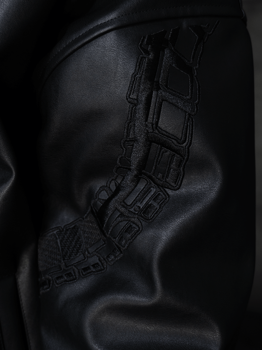 Close-up of the All-Black Eco Leather Nagamani Set by Machina - Wearable Technology, showing black leather with a raised, geometric textured pattern curving across its surface.