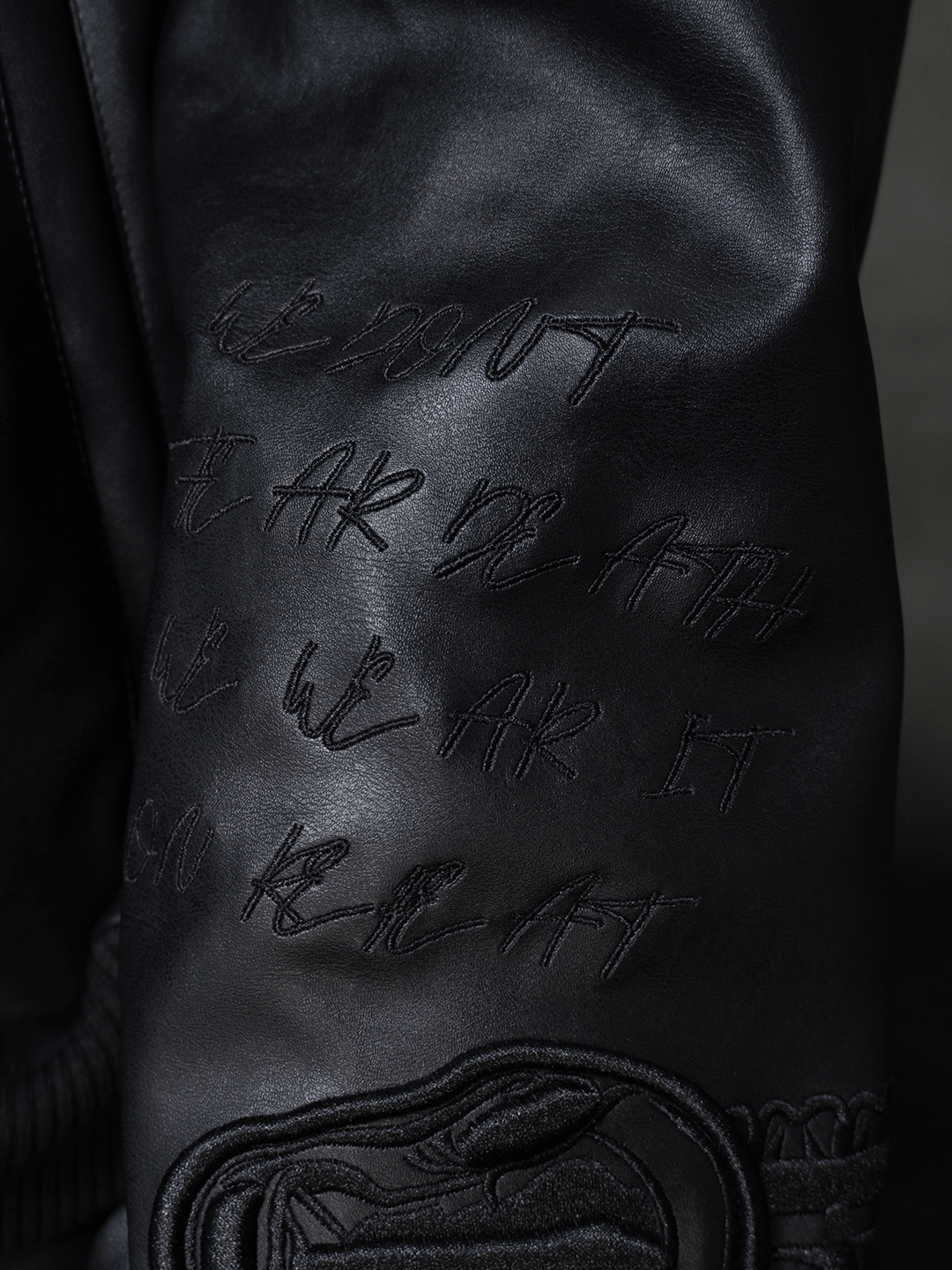 Close-up of the All-Black Eco Leather Nagamani Set by Machina - Wearable Technology, featuring black leather with embossed and embroidered script text and textured stitching details.