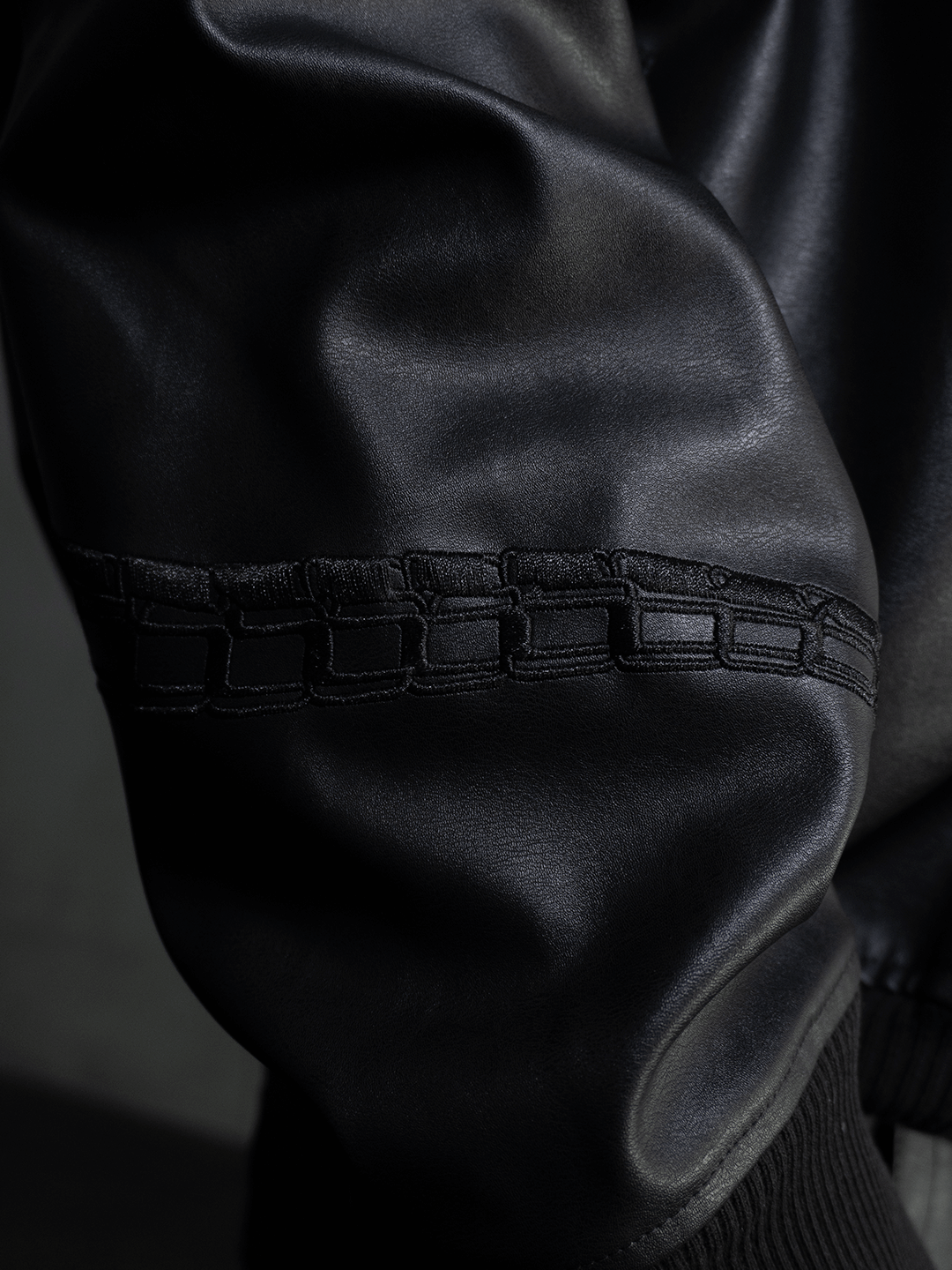 Close-up of the All-Black Eco Leather Nagamani Set by Machina - Wearable Technology, showing a black sleeve with decorative stitching near the seam and ribbed cuff detail.