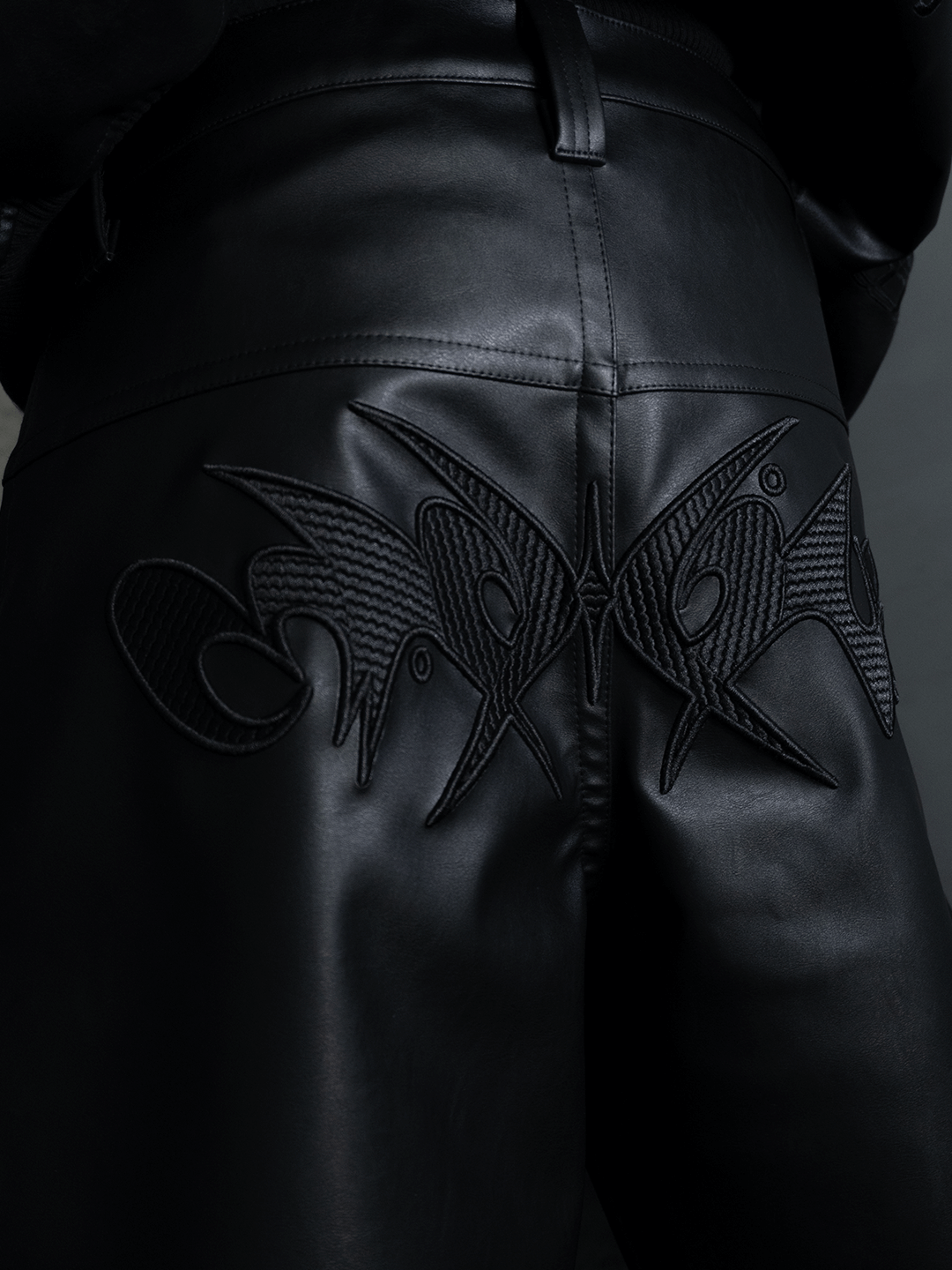 Close-up of the All-Black Eco Leather Nagamani Set by Machina - Wearable Technology, showing detailed black embroidery with abstract, angular patterns across the back.