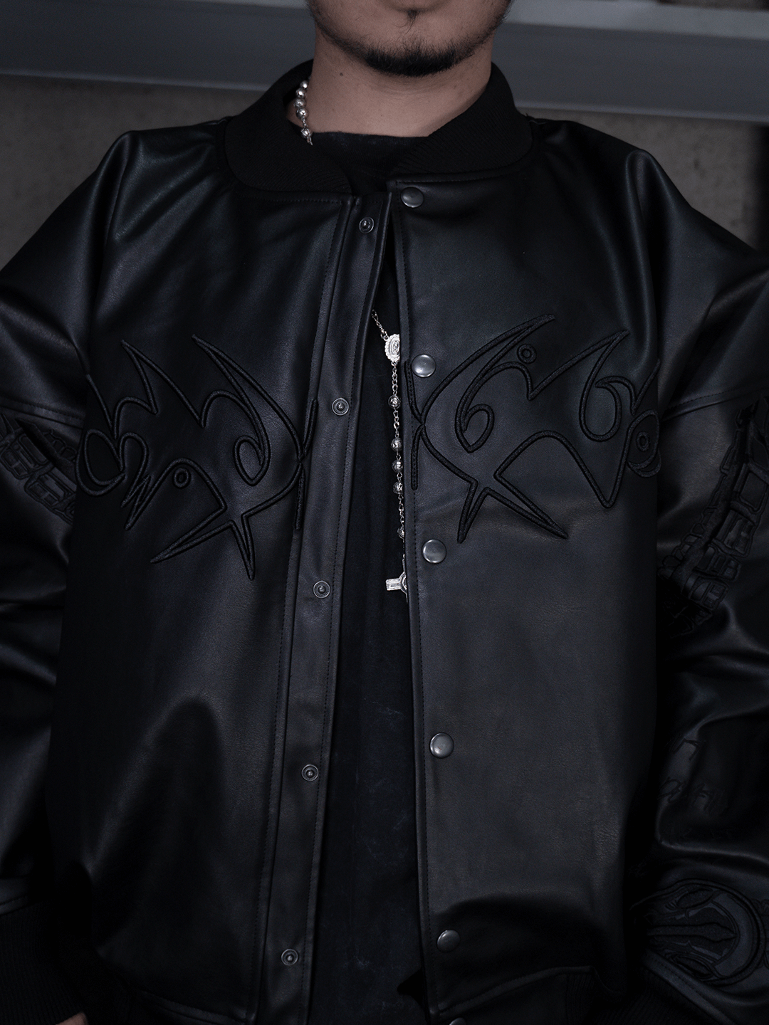 A person models the Machina All-Black Eco Leather Nagamani Set—featuring stylized embroidery—over a black shirt and silver chain. Cropped from shoulders to waist, the photo partially shows the face.