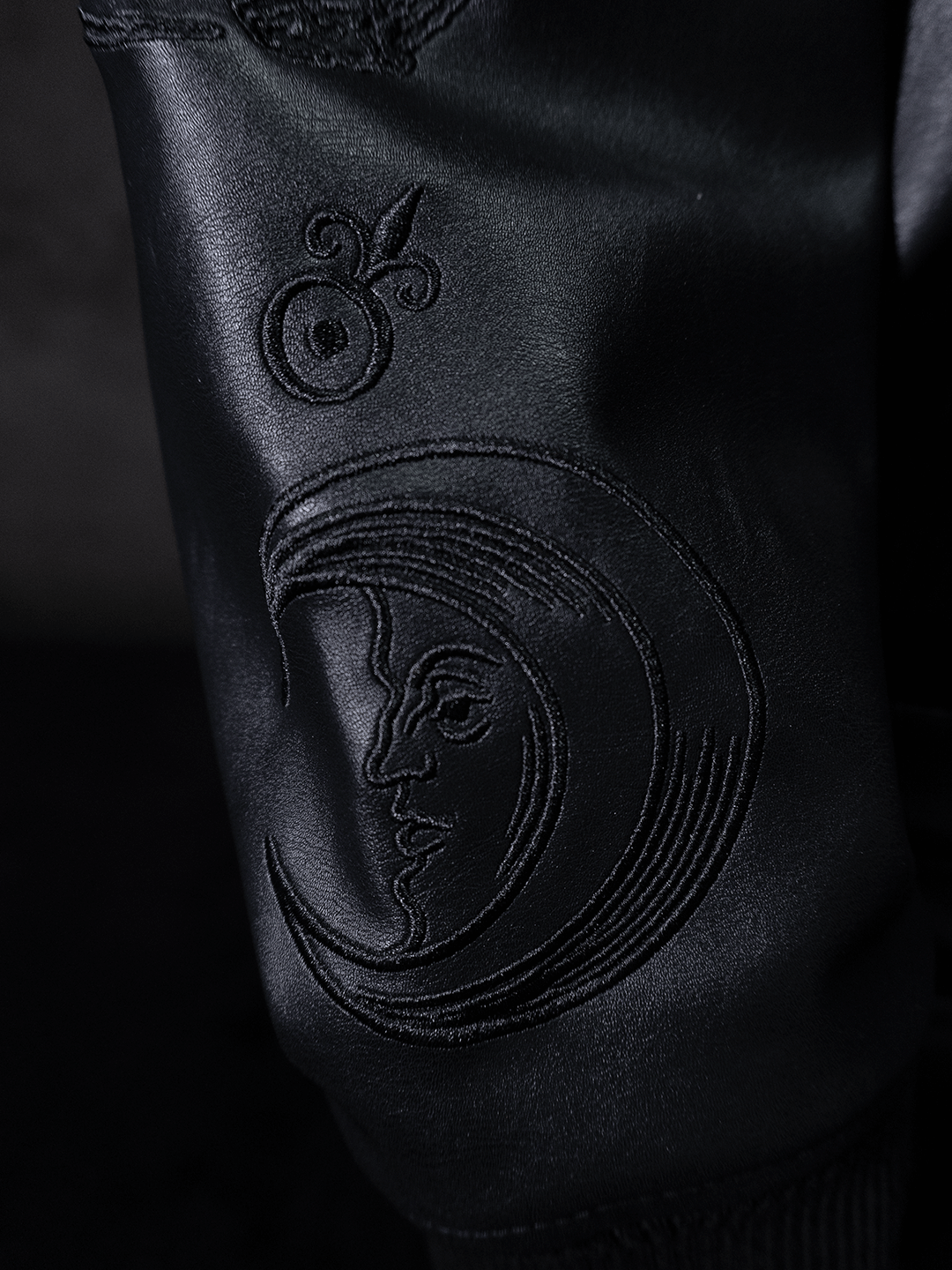 The All-Black Eco Leather Bubble Set by Machina - Wearable Technology features black leather with embroidered designs, including a crescent moon face and an abstract circle, all stitched in black thread.