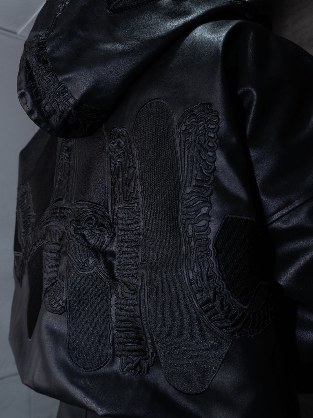 A close-up of a person wearing the Machina - Wearable Technology All-Black Eco Leather Osseous Full Zipper set, featuring bold, textured embroidery and stitched patterns in black for an artistic, ceremonial armor-inspired look.