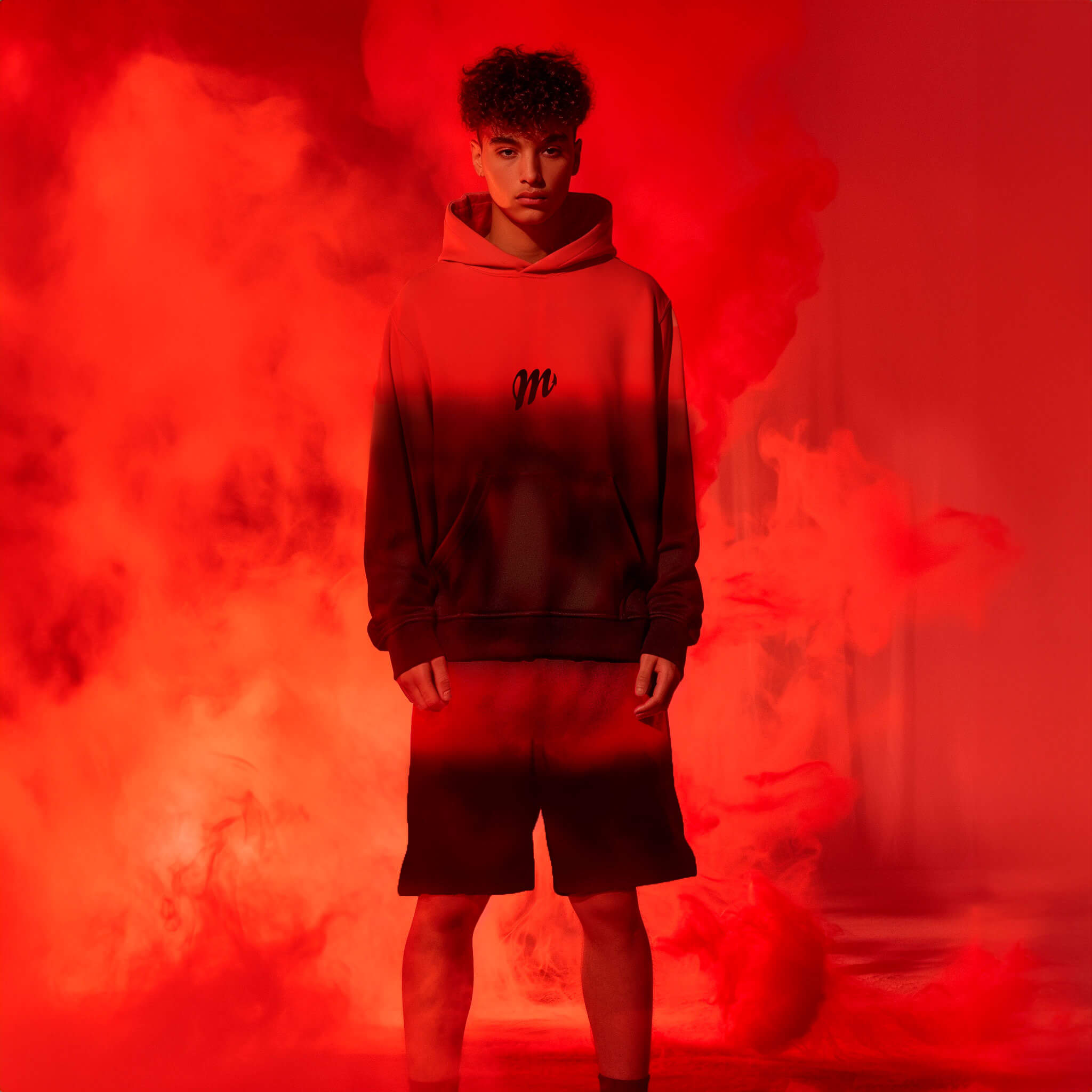 In a dimly lit room filled with thick red smoke, a person models a Crimson Hoodie and matching shorts from Machina - Wearable Technology, staring intently at the camera. The scene is both dramatic and intense.