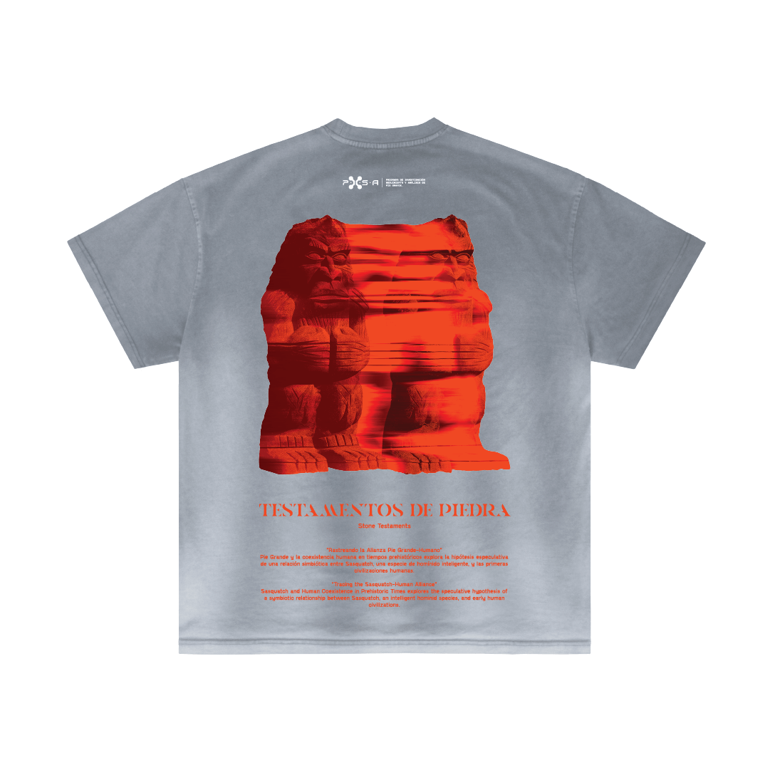 A gray t-shirt by Machina - Wearable Technology, showcasing a prominent red, digitally-rendered stone sculpture with the text "Testamentos de Piedra" beneath it. The shirt also features subtle hints of an ancient alliance in the additional text underneath.