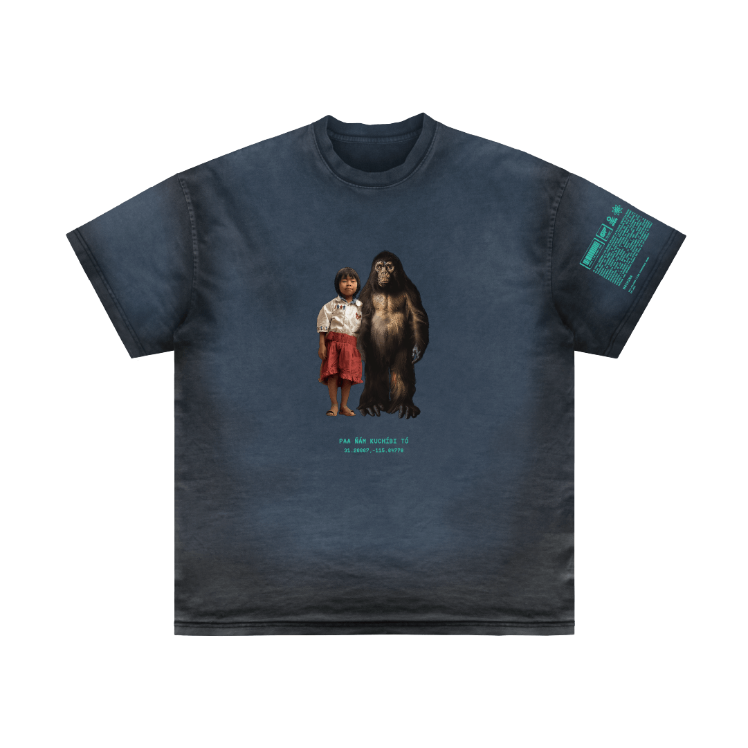 A dark-colored T-shirt with a graphic of a young boy alongside Bigfoot, titled "Valle de los Gigantes" by Machina - Wearable Technology. Text beneath the image and on one sleeve contrasts the plain background, emphasizing the central illustration.