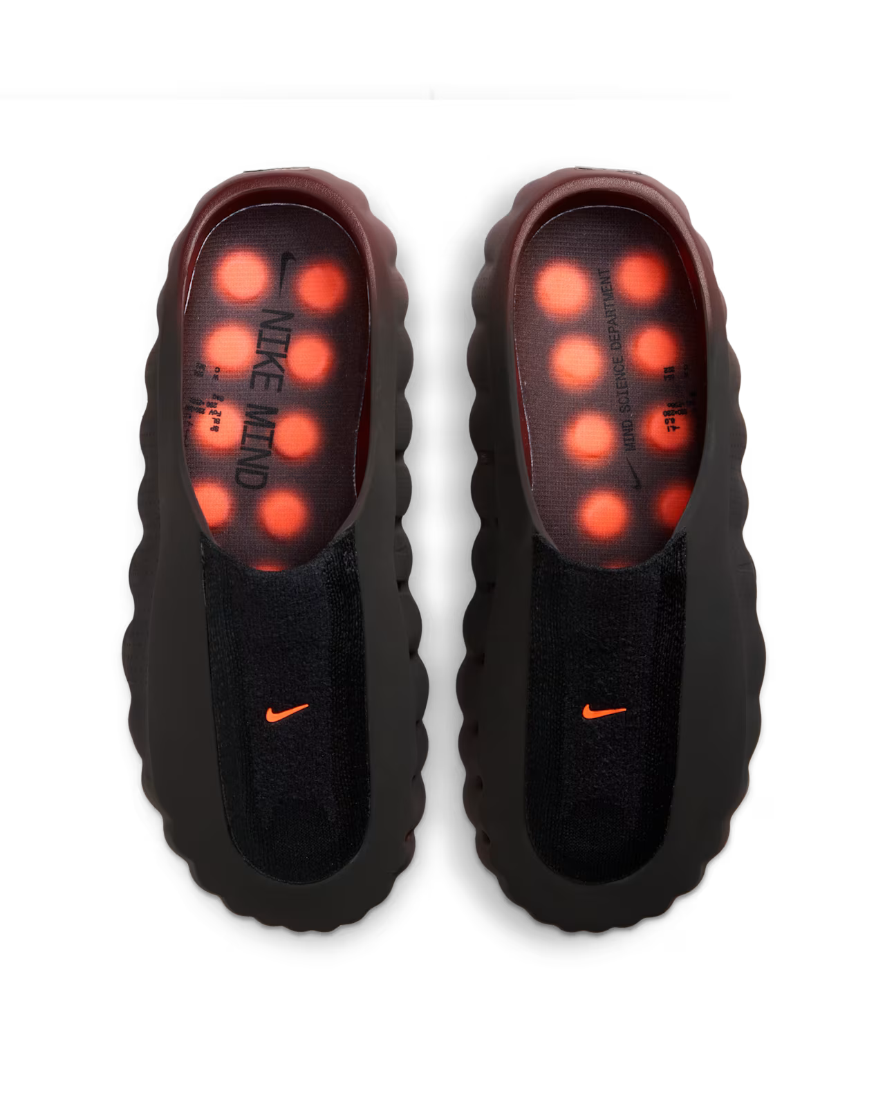 A pair of black Mind 001 Flyknit Bronze Eclipse slip-on shoes by Machina Wearable Technology, with wavy edges, orange logos, visible orange cushioning dots in the soles, and “NIKE MIND” text on the insoles. Viewed from above.