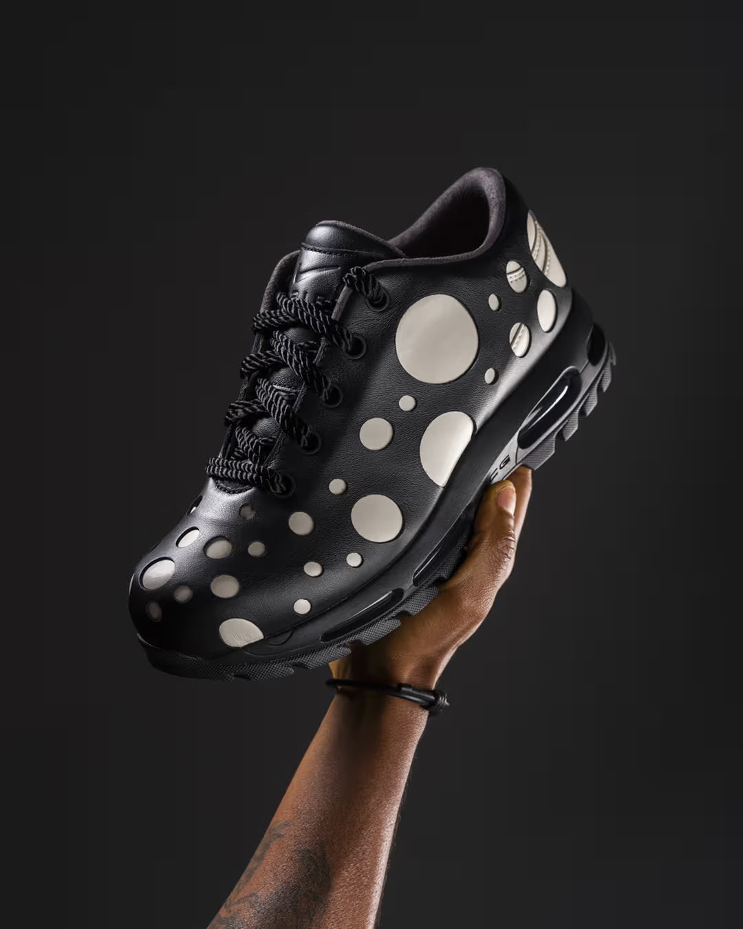 A hand holds up a Machina Wearable Technology Air Max Goadome Low sneaker in Light Orewood Brown and Black, set against a dark background.