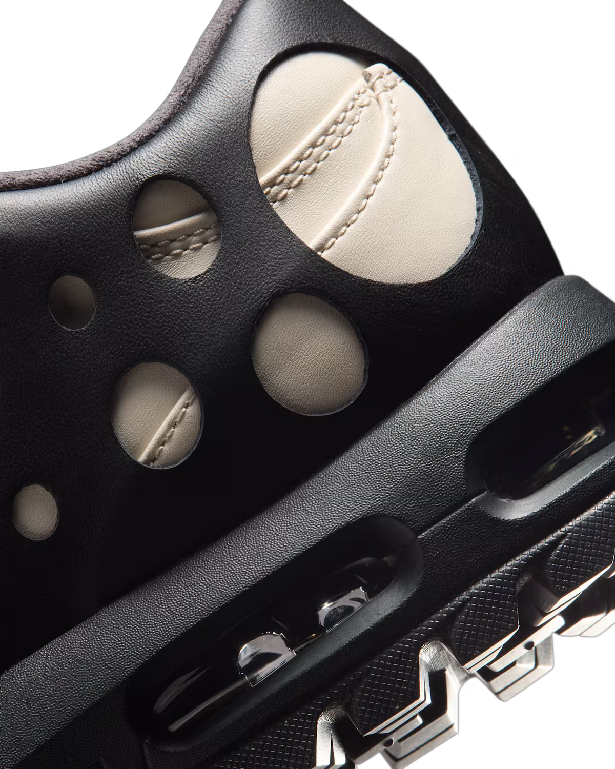 Close-up of the Machina Wearable Technology Air Max Goadome Low sneaker in Light Orewood Brown and Black, highlighting its black upper with circular cutouts that reveal light beige fabric beneath, refined stitching details, and a chunky black sole featuring visible air cushioning and durable tread. The neutral palette and rugged construction channel the spirit of an outdoor boot, merging contemporary style with lasting durability.