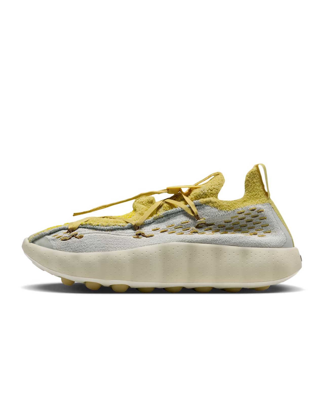 A light bone and saturn gold Machina Wearable Technology Mind 002 sneaker featuring a textured upper, distinctive lacing system, and a thick, wavy cream-colored sole. This modern lifestyle footwear showcases a sporty design and is displayed in a side profile on a white background.