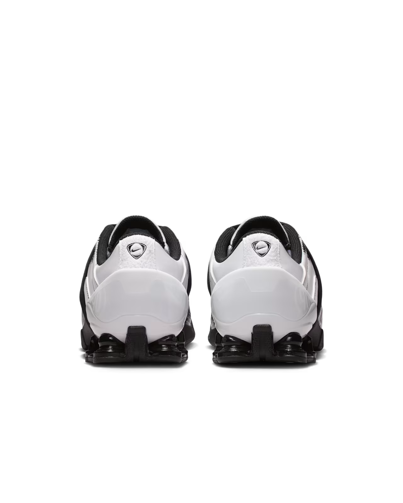 A pair of Machina Wearable Technology Total 90 Shox Magia White and Black athletic sneakers viewed from the back, highlighting the heel and sole design with a small logo on each heel.