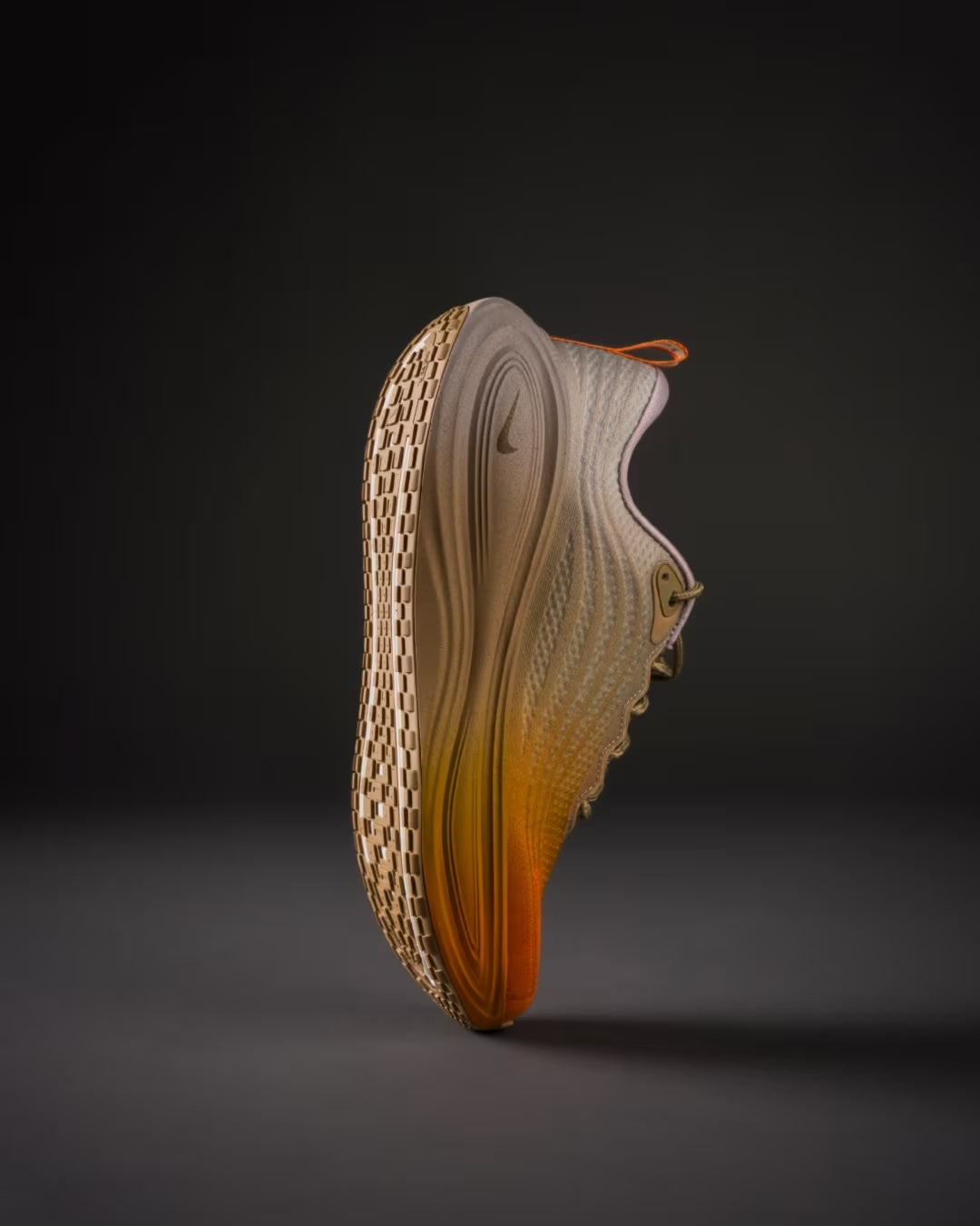 A single Nike Vomero Plus “Cheat Day” running shoe from Machina Wearable Technology, in beige and orange, stands on its heel against a dark background. Its textured sole and curved design are prominent, with a small Swoosh logo visible near the laces.