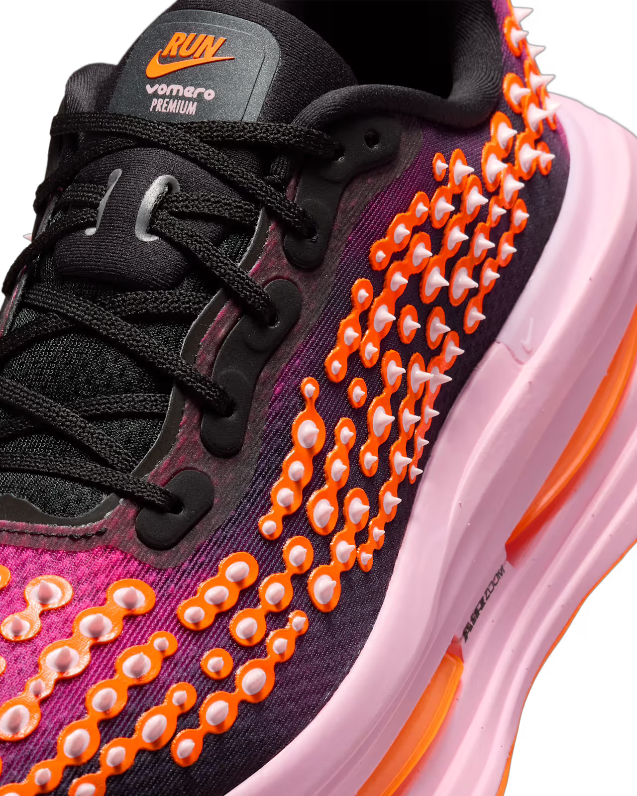 A close-up of the Machina Wearable Technology Nike Vomero Premium “Otaku Approved” sneaker showcases vibrant black, pink, and orange accents, highlighted by raised orange and white dot details along the side. Its thick pink and orange sole takes cues from high-cushion running shoes, blending plush comfort inspired by the Nike Vomero Premium with bold references to the ZoomX platform.