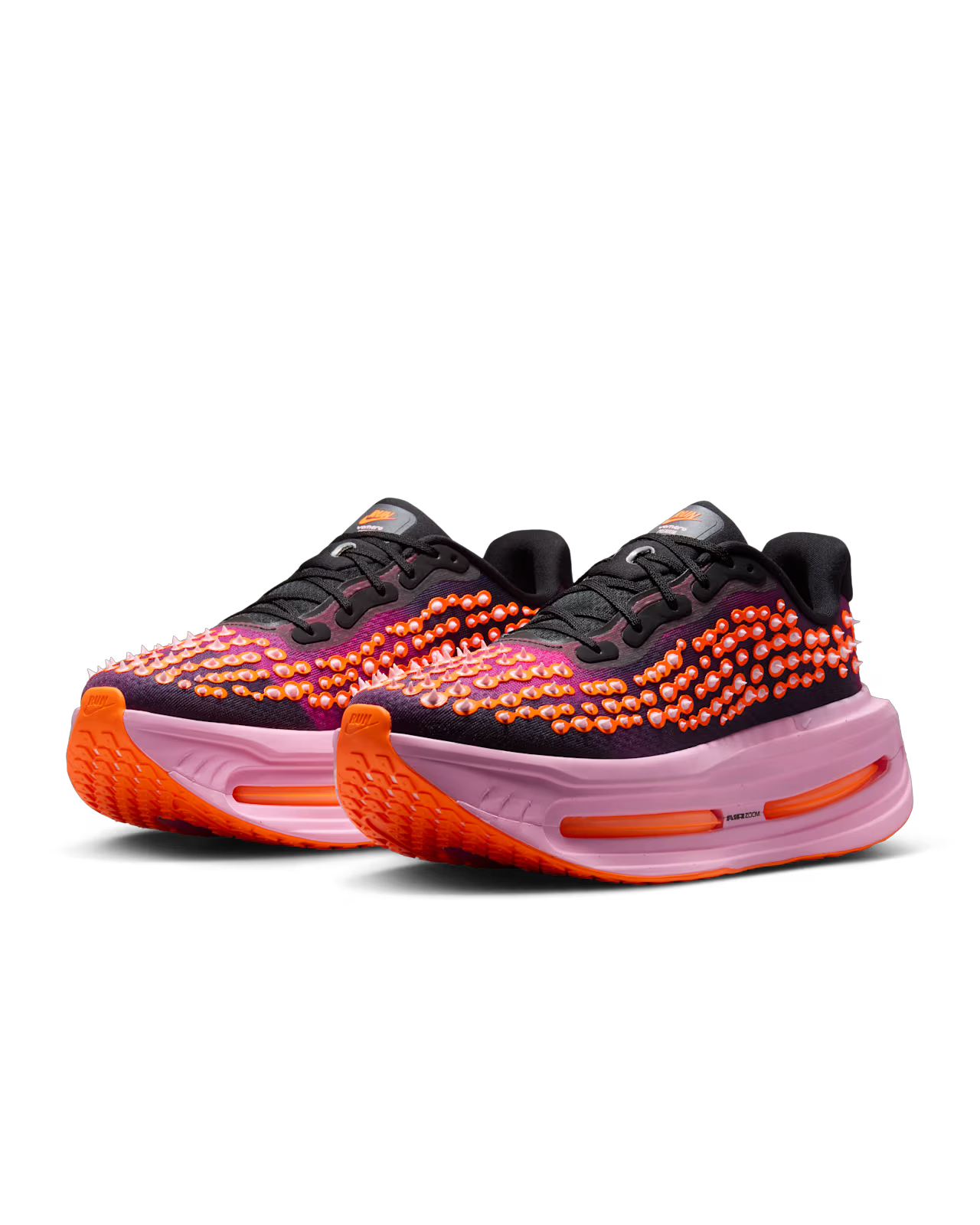A pair of The Nike Vomero Premium “Otaku Approved” sneakers by Machina Wearable Technology, featuring black uppers, bold pink and orange bubble accents, thick light pink midsoles with the ZoomX platform for maximum cushioning, and vibrant orange outsoles—shown against a white background.