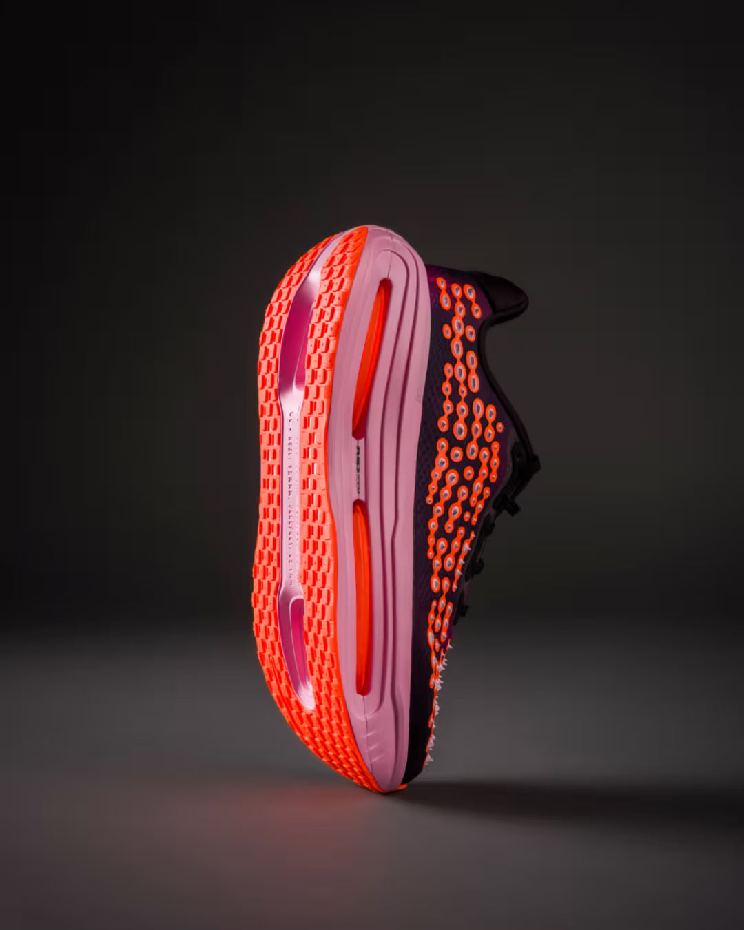 The Nike Vomero Premium “Otaku Approved” by Machina Wearable Technology showcases a bold bright orange honeycomb-patterned sole and side, features the innovative ZoomX platform for superior responsiveness, and is accented with a striking purple midsole and sleek black upper—all presented vertically against a dark backdrop.