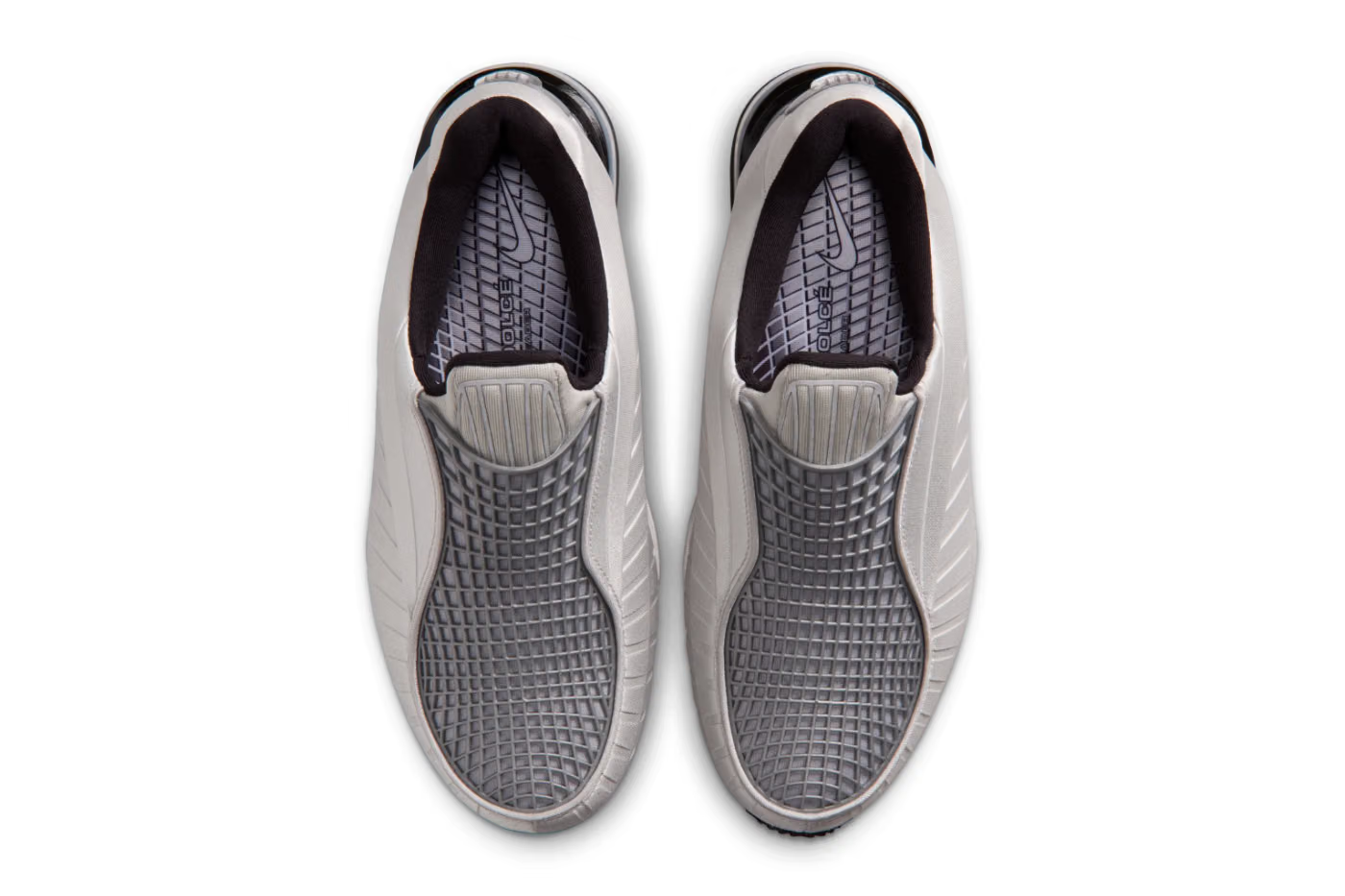The Nike Air Max Dolce “Metallic Silver” by Machina Wearable Technology features slip-on lifestyle sneakers in light gray with textured, grid-patterned uppers and cushioned insoles. Seen from above on a white background, subtle Metallic Silver accents add a modern edge to the streamlined design.