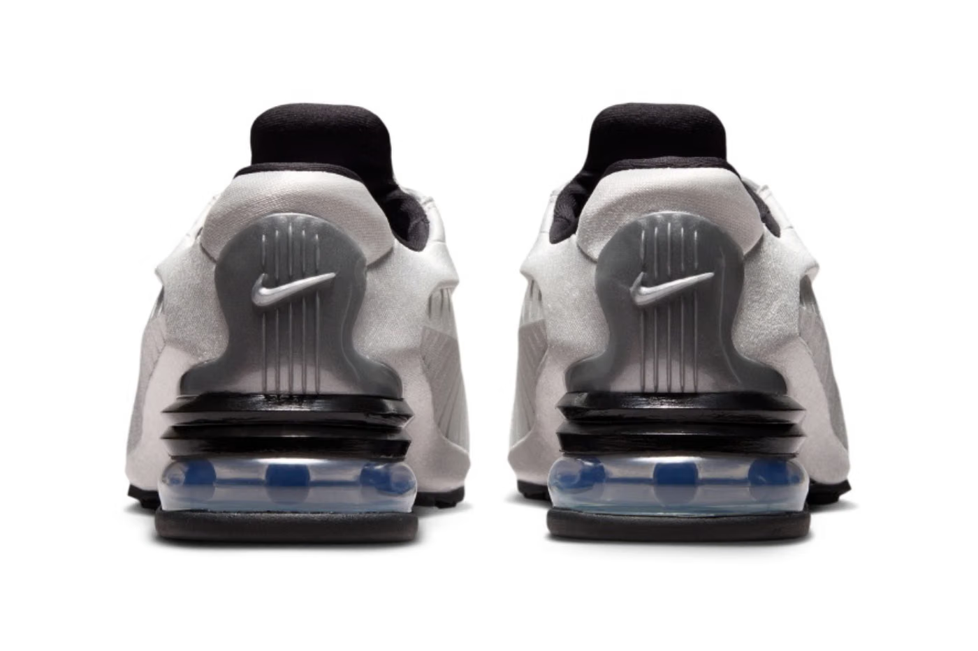 Rear view of two white Machina Wearable Technology Nike Air Max Dolce “Metallic Silver” lifestyle sneakers with visible blue air cushions in the black soles and metallic silver Nike swooshes on the heels, set against a white background.