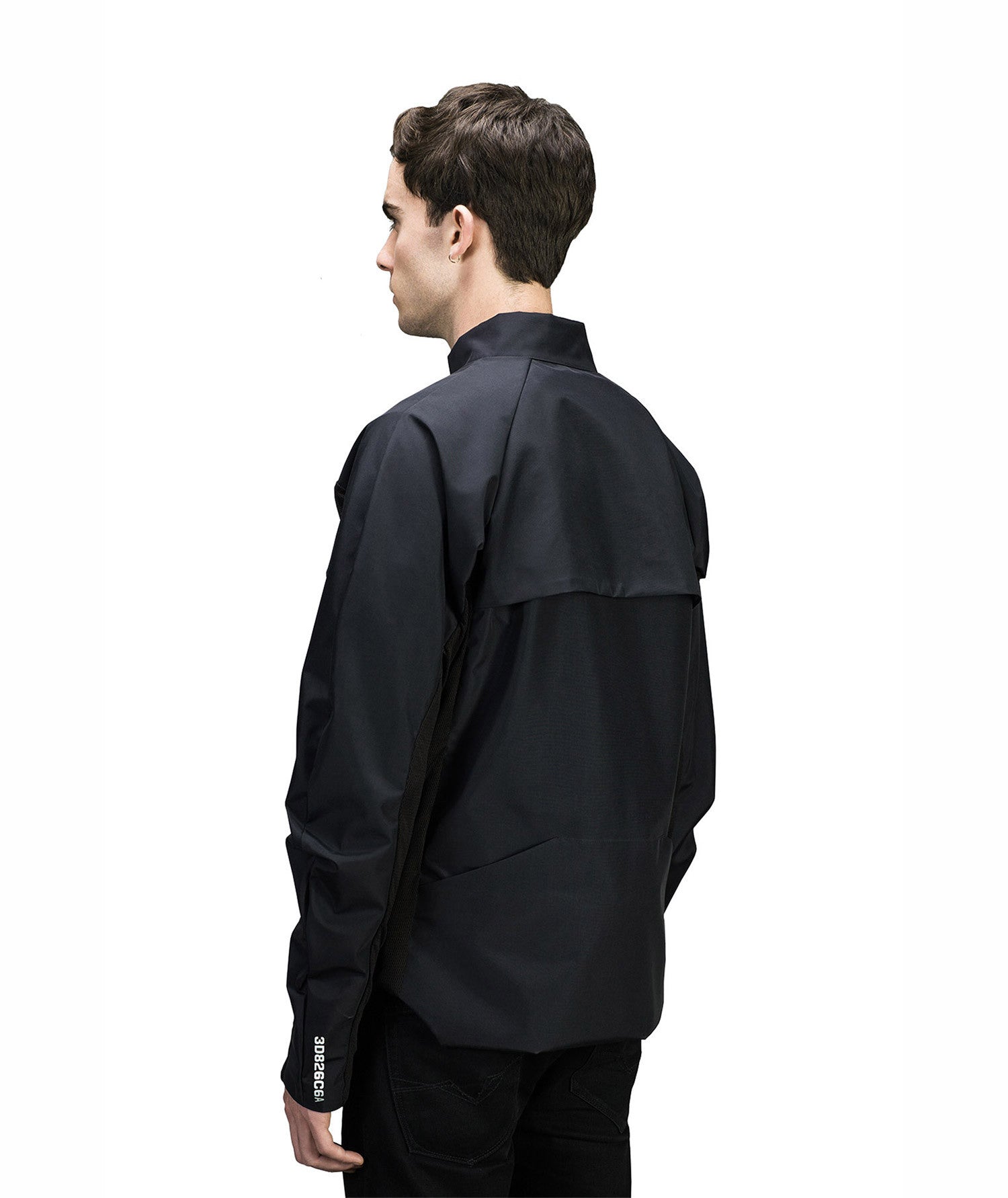 A person with short dark hair is wearing a stylish black MIDI Jacket by Machina - Wearable Technology, facing away from the camera. The minimalist design includes a discreet logo on the sleeve. The plain white background highlights the innovative blend of fashion and technology for music creators.