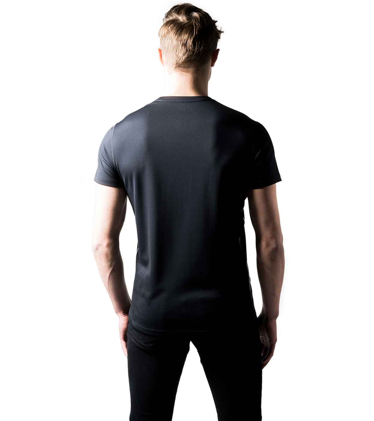 A person is facing away from the camera, dressed in a Smart Black T-shirt from Machina - Wearable Technology and dark pants. The all-white backdrop emphasizes their choice of eco-friendly fashion.