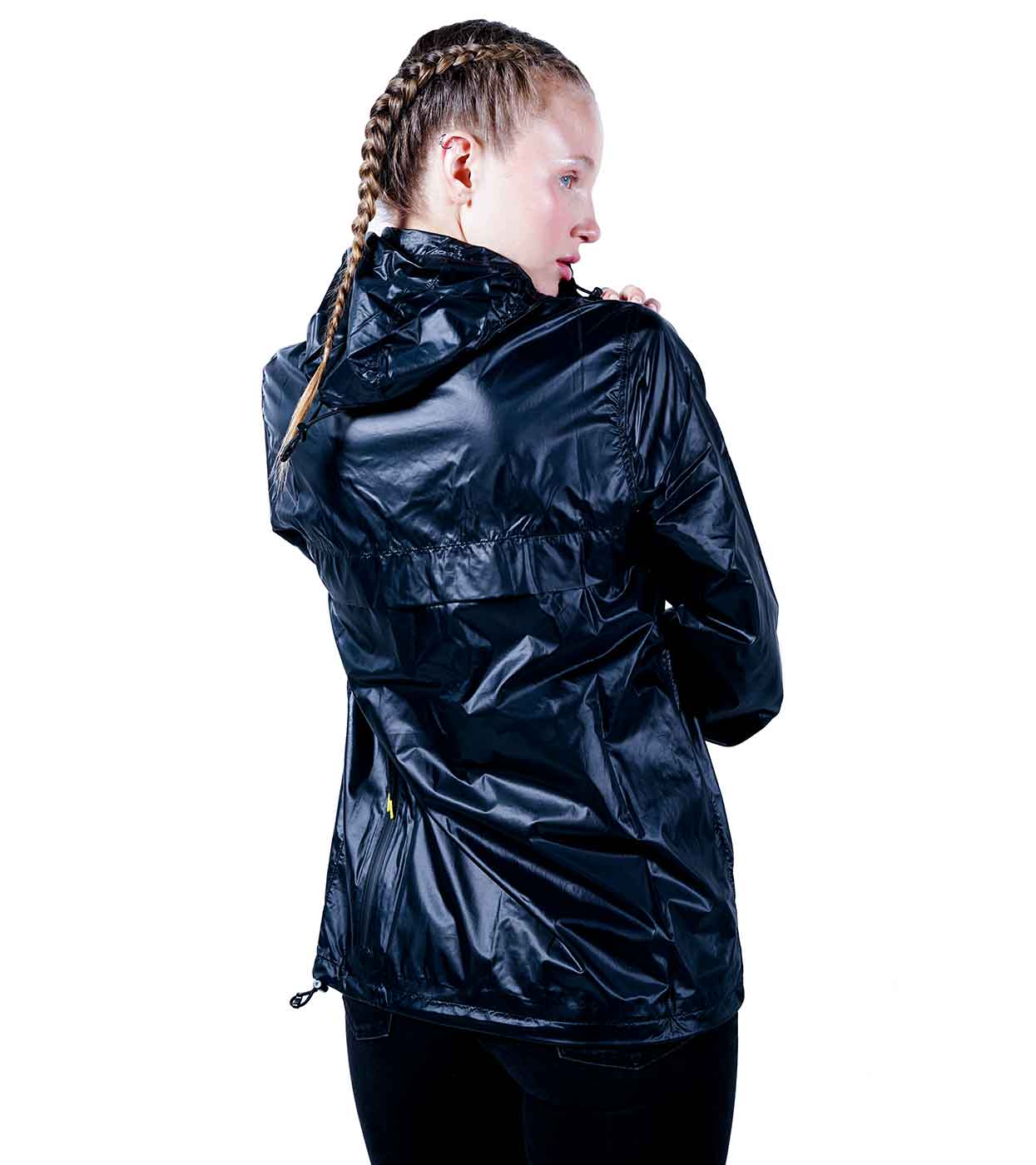 A person with braided hair, wearing the glossy BLACK WINDBREAKER by Machina - Wearable Technology, glances over their shoulder. They stand against a white background, accentuating the jacket's shiny finish and showcasing the pinnacle of fashion technology.
