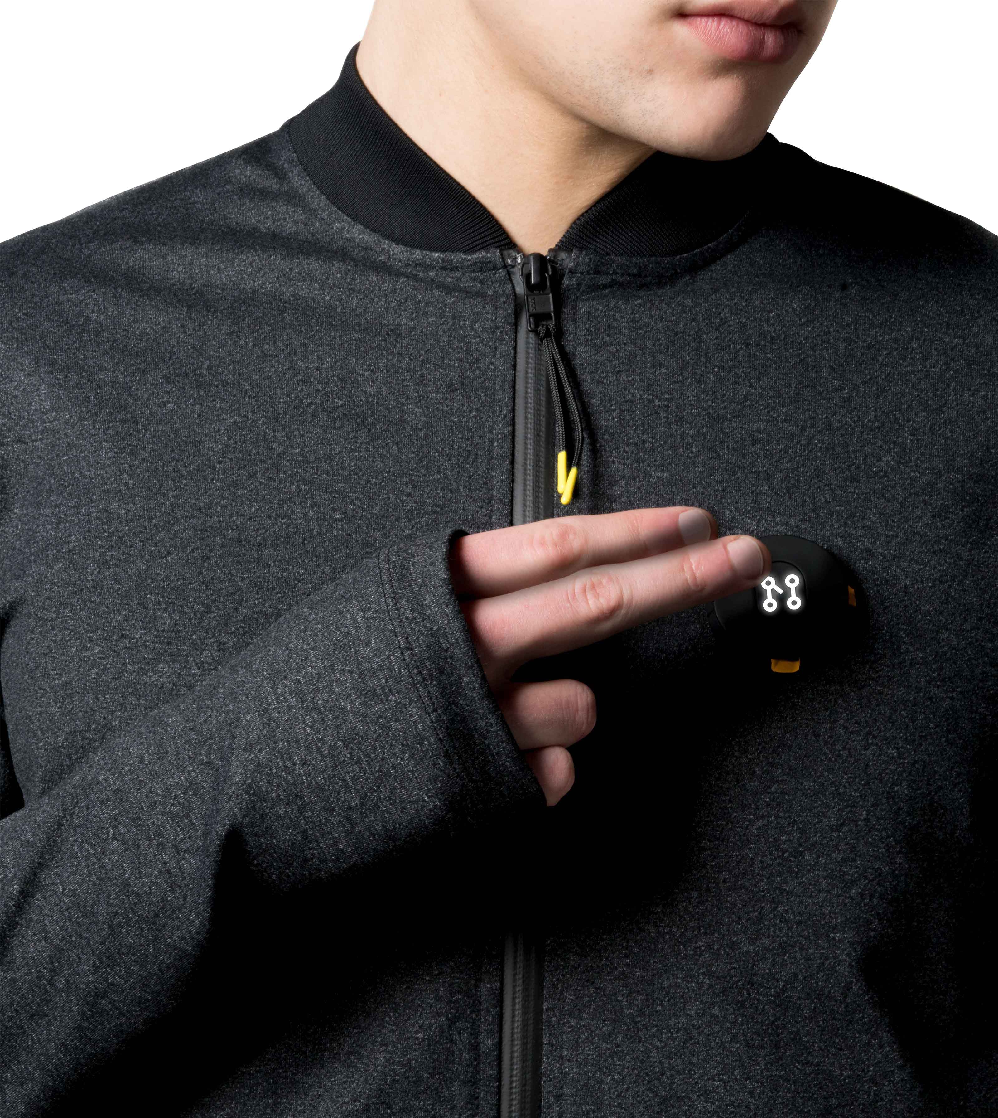 Dressed in a BLACK BOMBER JACKET by Machina - Wearable Technology, an individual holds a sleek black gadget with illuminated symbols close to their chest. This compact device exudes a futuristic vibe, effortlessly merging cutting-edge innovation with fashion tech.