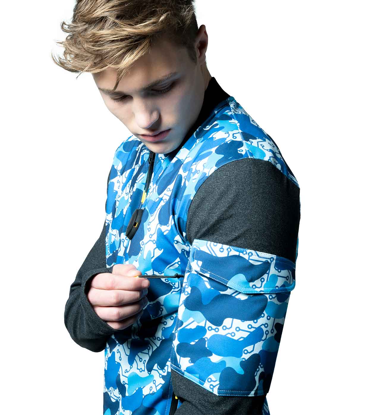 A person sporting the BLUE-CAMO BOMBER JACKET by Machina - Wearable Technology adjusts the sleeve. The jacket boasts an abstract wave-like design in blue and black, crafted from eco-friendly materials, and is worn over a black long-sleeve top against a plain white background.