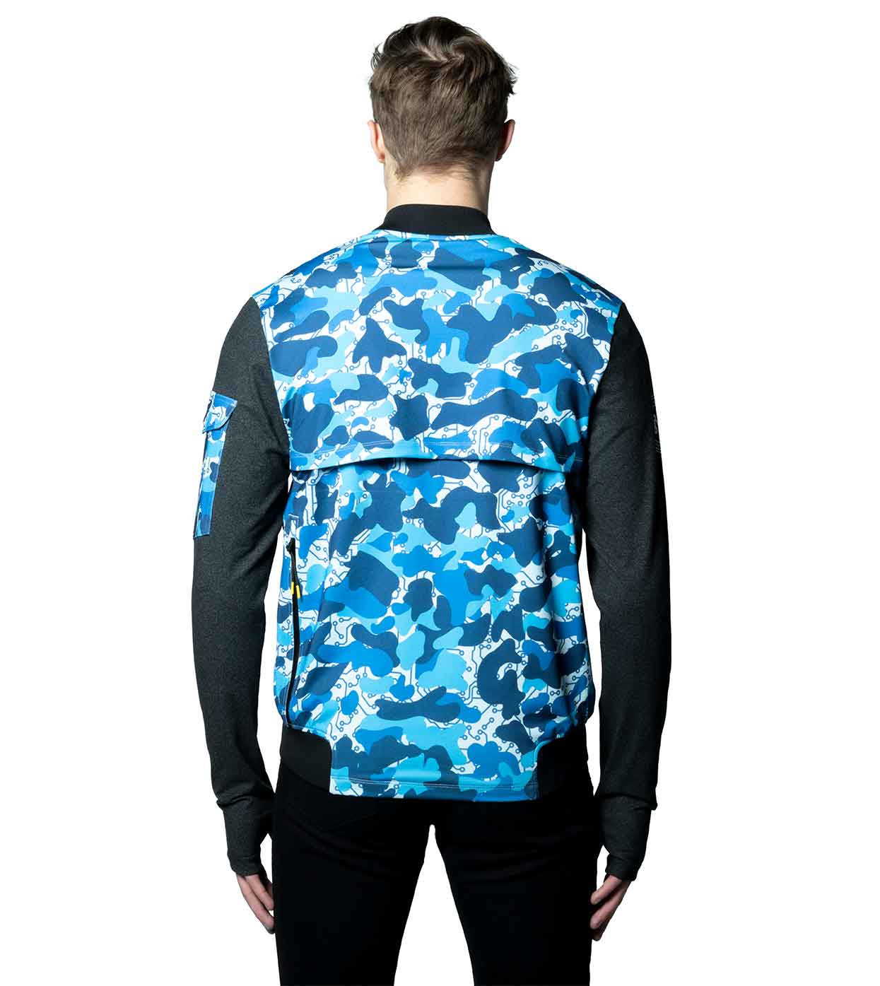 A person stands with their back to the camera, wearing the Machina - Wearable Technology BLUE-CAMO BOMBER JACKET, which showcases a distinctive blue and white camo pattern coupled with black sleeves. This smart bomber jacket is made from sustainable fabrics and features a unique flap detail on the upper back, set against a plain white background.