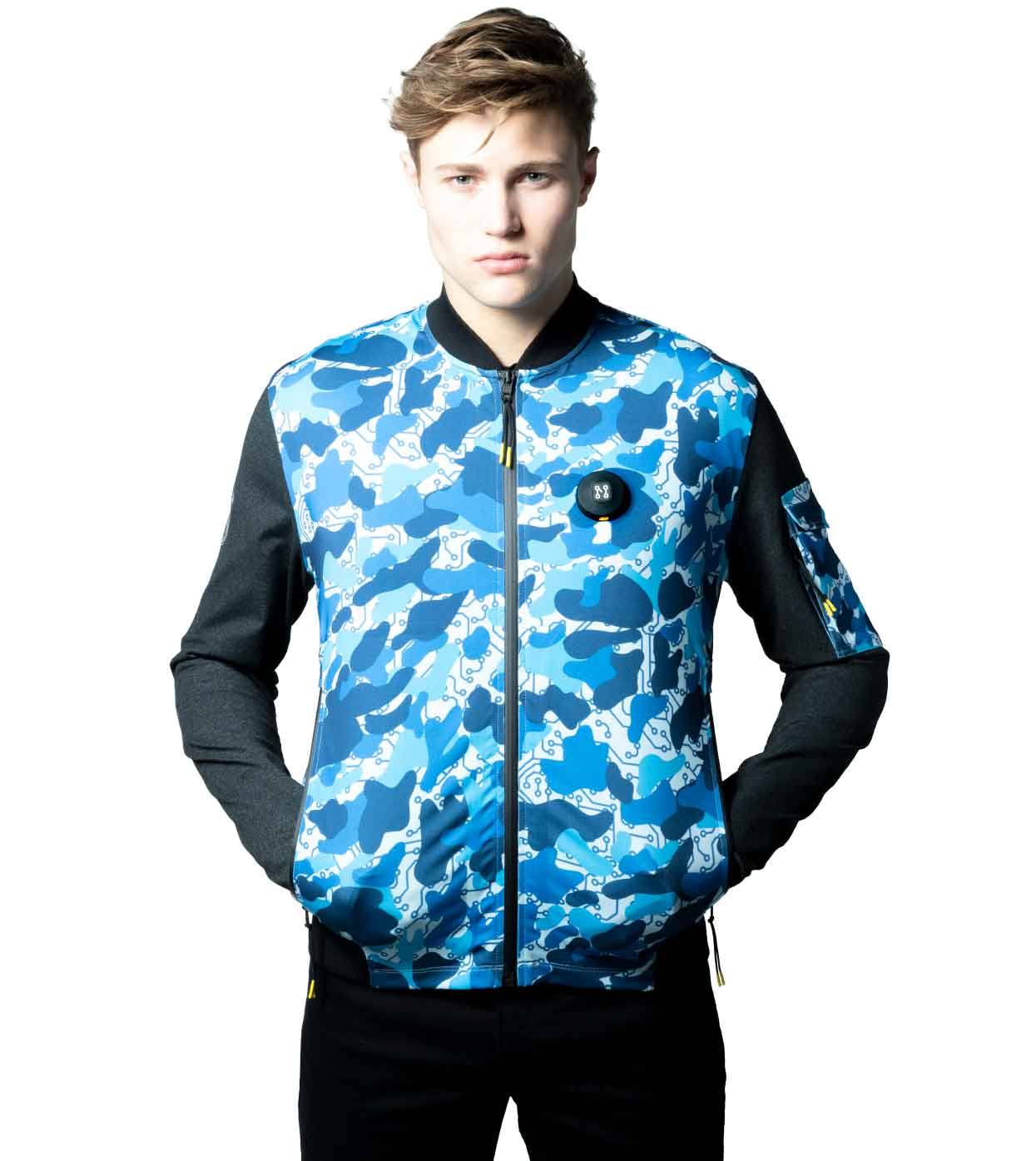A person is pictured wearing the BLUE-CAMO BOMBER JACKET by Machina - Wearable Technology, showcasing a blue and white camouflage design made from sustainable materials. With short brown hair, they stand against a plain white background with their hands in their pockets, effortlessly blending style and innovation.