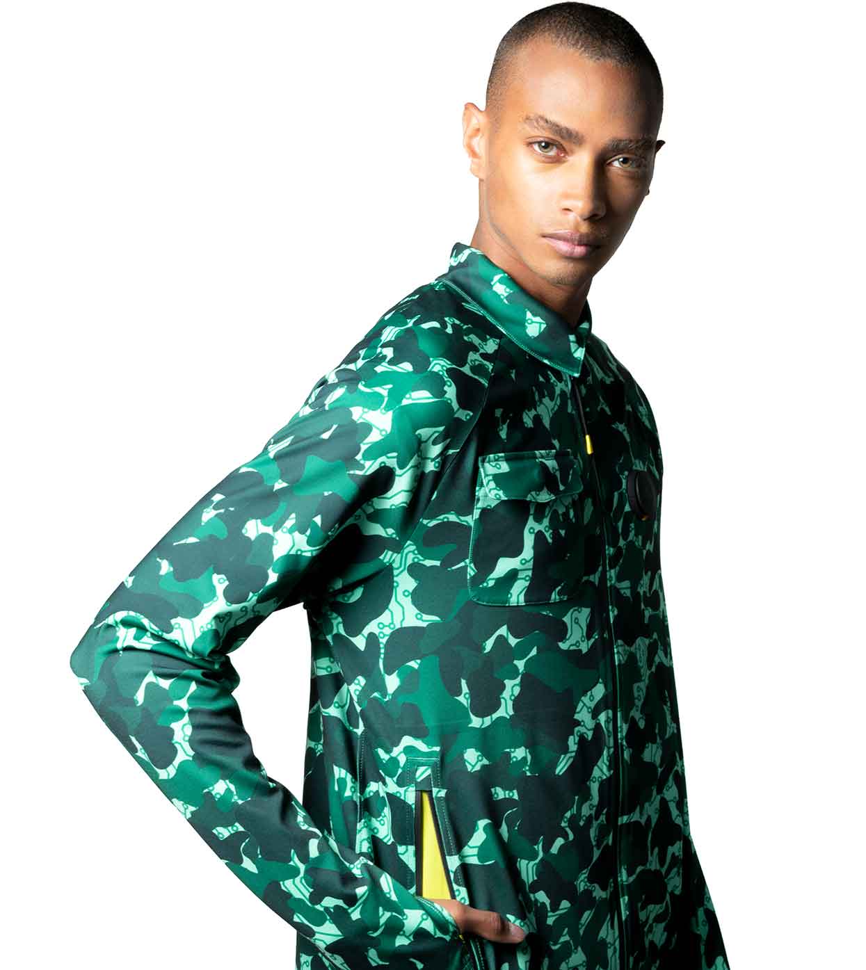 A person confidently poses in an AQUA-CAMO CASUAL JACKET by Machina - Wearable Technology, set against a white background. This smart casual jacket, featuring fashion technology, includes a zippered front and two breast pockets. They effortlessly merge style and innovation while standing with one hand in a side pocket.