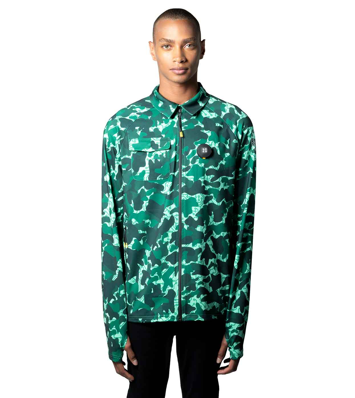 A person dressed in the AQUA-CAMO CASUAL JACKET by Machina - Wearable Technology poses against a plain white backdrop. This smart casual jacket, crafted from sustainable fabrics, showcases a striking green and white camouflage design, a zip-up front, and features a small patch on the left side. With a neutral expression, they gaze directly at the camera.
